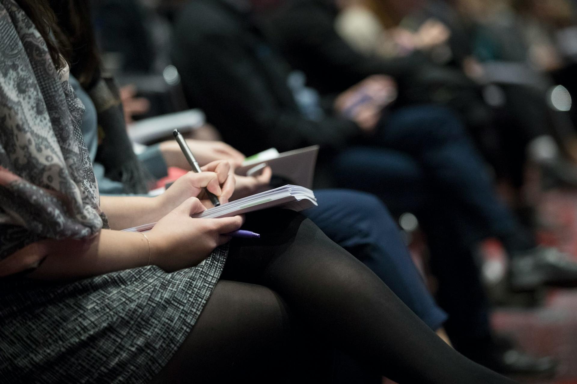 people sitting in an audience writing things down