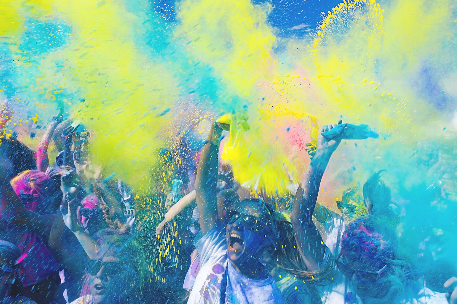 A group of people shouting and throwing green, pink, and blue colored dust in the air in this image for a Meltwater customer story about Energy PR.