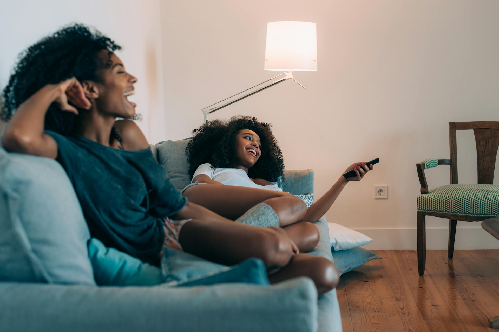 Two women sitting on a softa casually, with one pointing a TV remote control