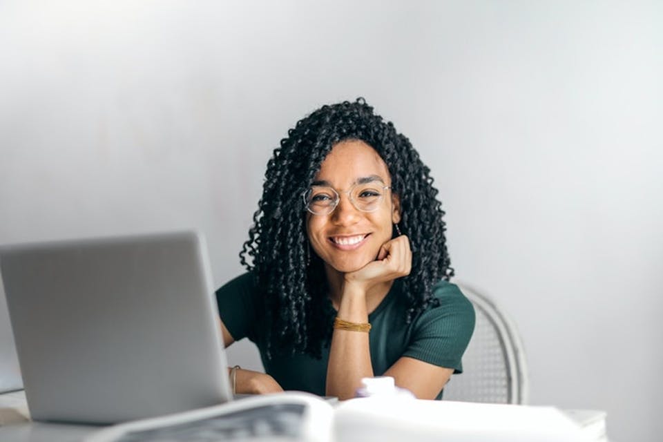 A young woman sitting in front of her laptop smiling into the camera. This is the header image of our blog about Why Branding & Brand Management Are a Must-Have for Your Business