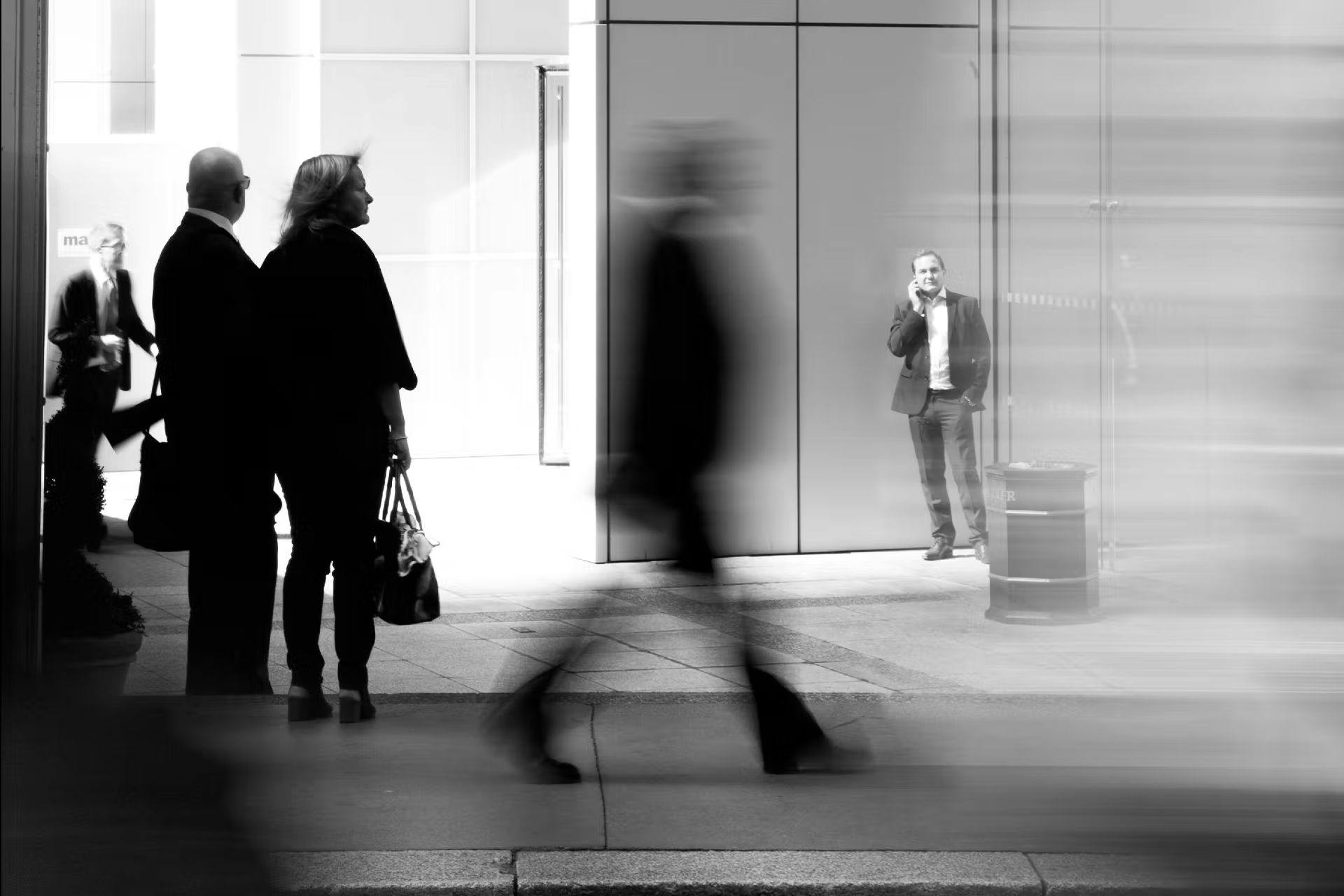 Photo en noir et blanc de personnes dans la rue. Trois personnes sont debouts, statiques et une marche - elle est floue