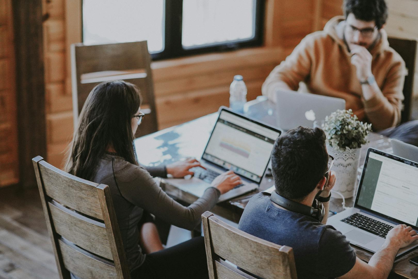 An image of three co-workers with their laptops, sitting around a table