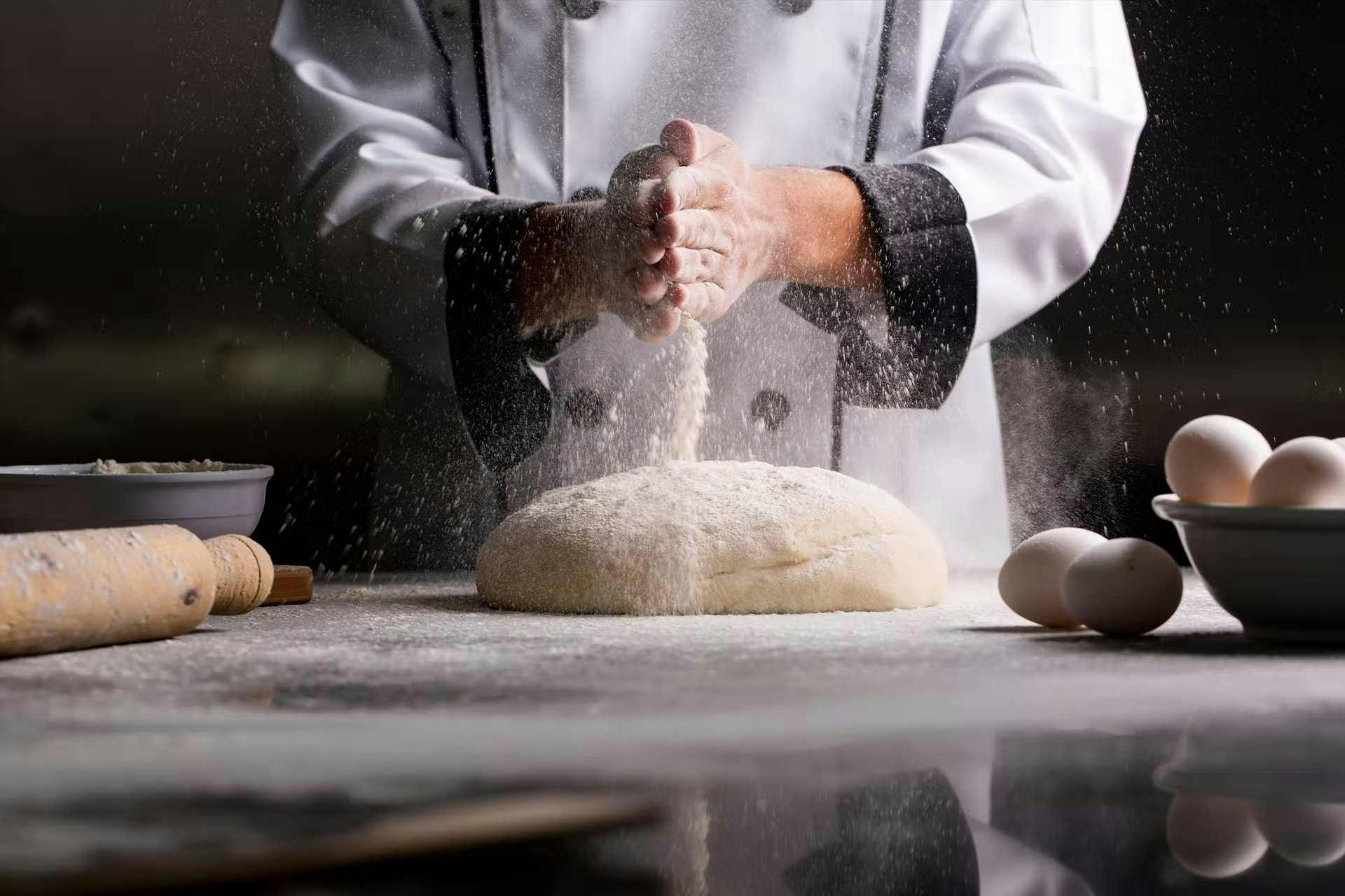 Boulanger devant son plan de travail qui met de la farine sur une boule de pâte
