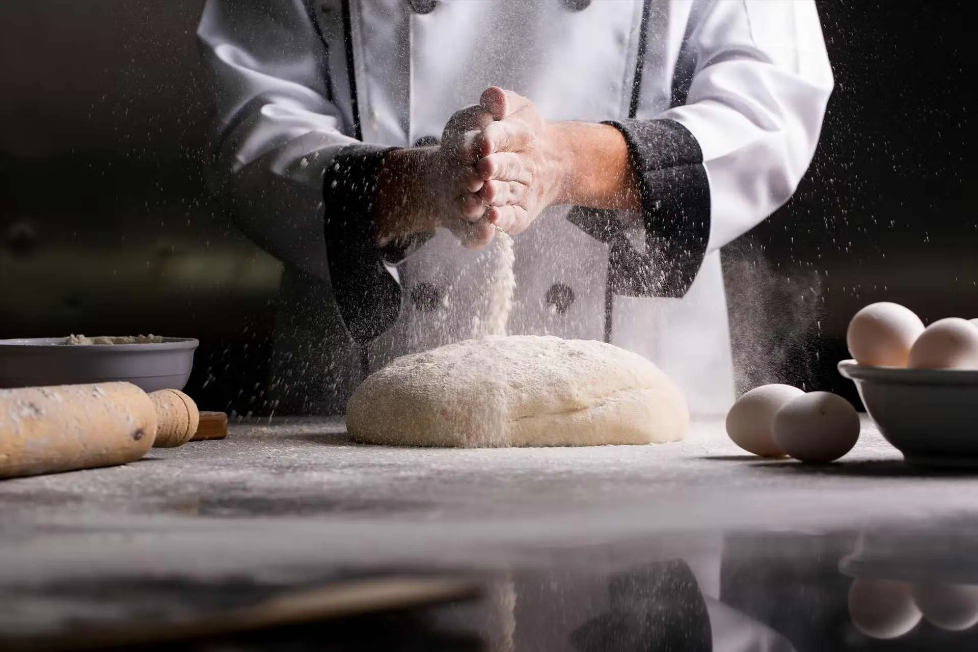 Boulanger devant son plan de travail qui met de la farine sur une boule de pâte