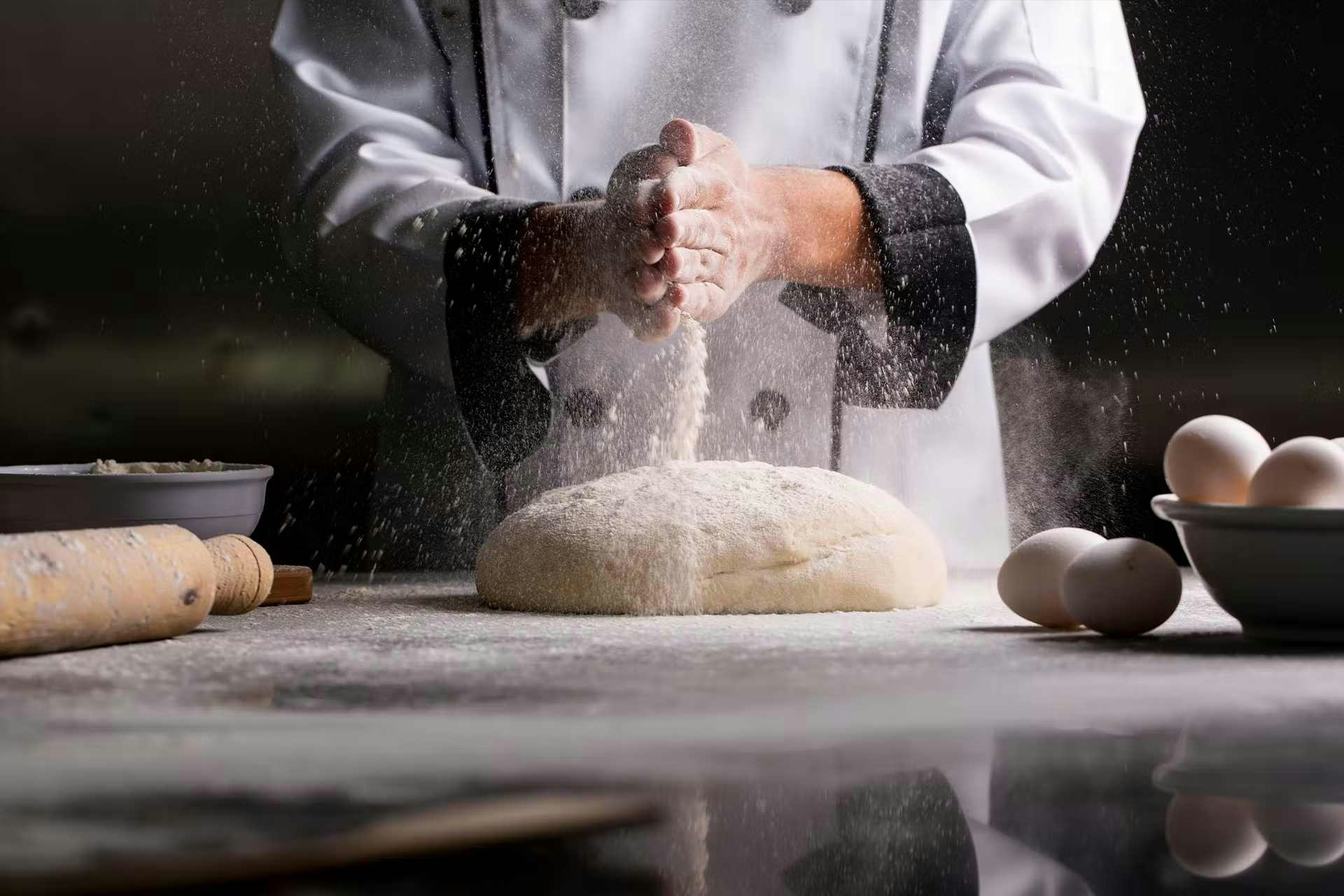 Boulanger devant son plan de travail qui met de la farine sur une boule de pâte 
