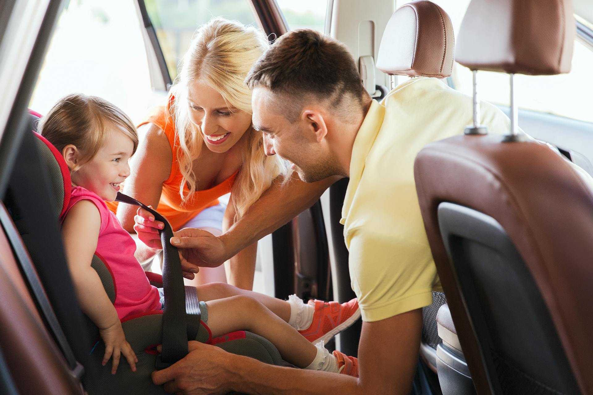 Photo of a small family in a car putting the seatbelt on their little daughter