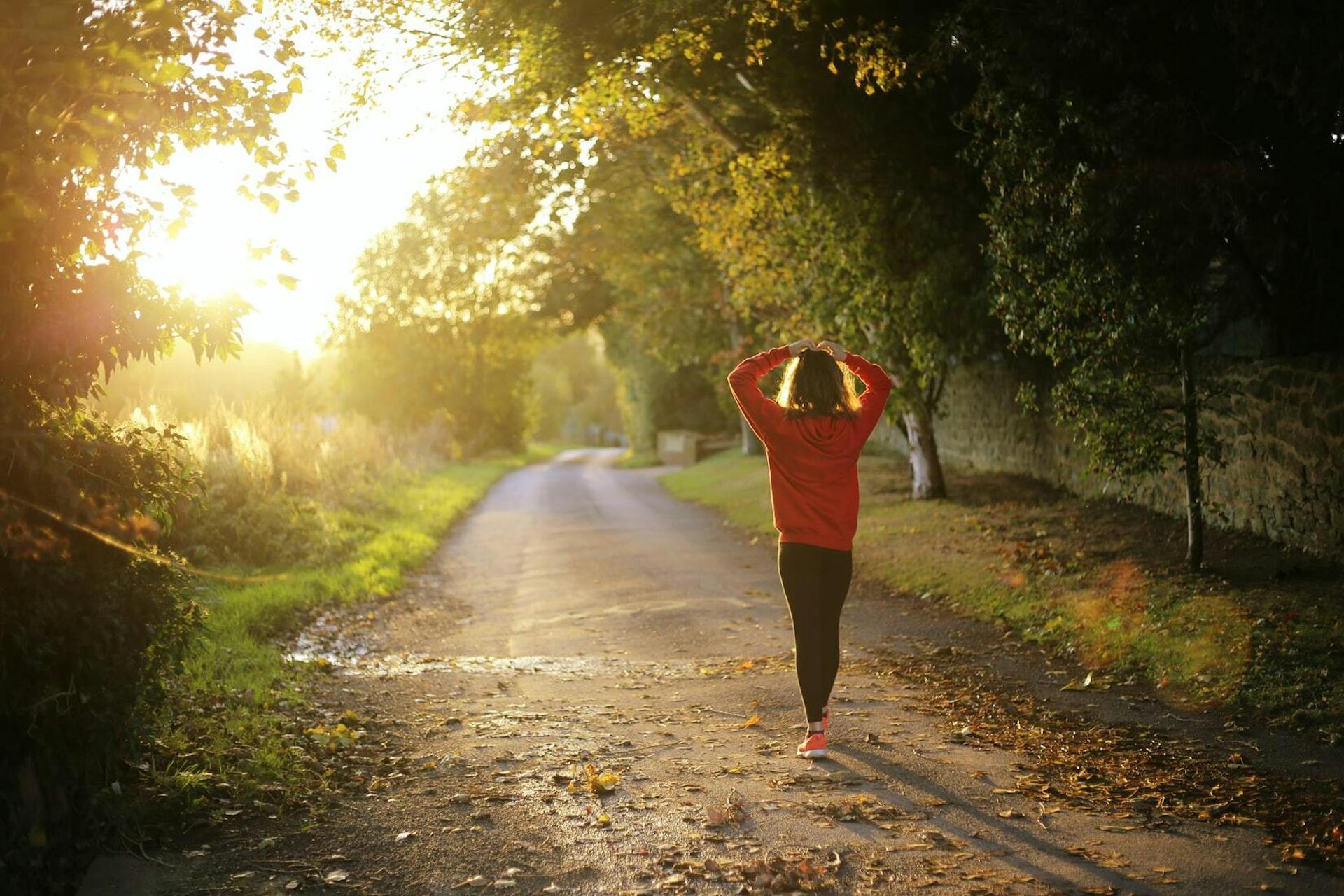 Woman in red jacket walking next to the forest into sunset