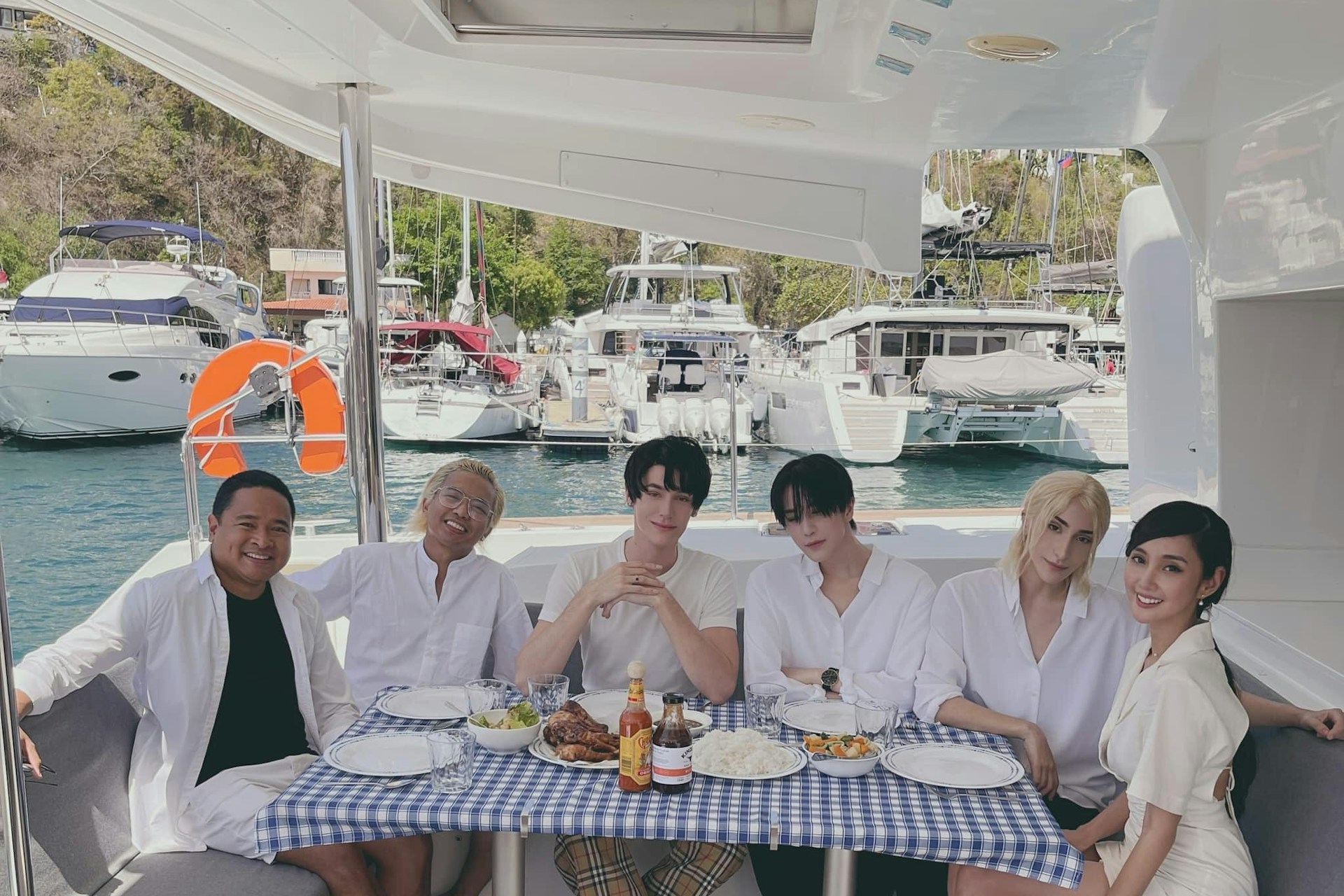 Six individuals, five male and one female sitting in a yacht smiling and taking a picture