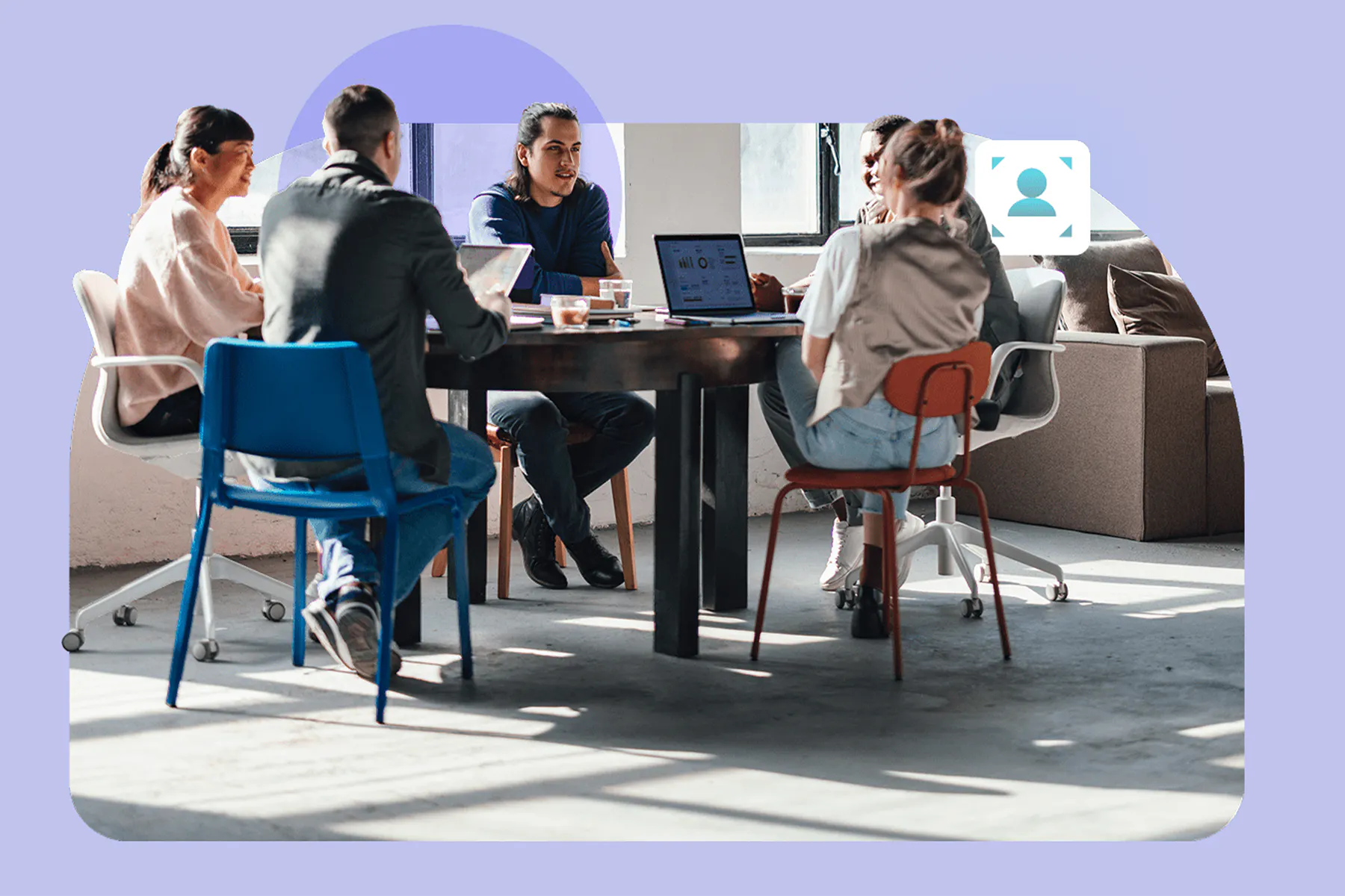 A photo of a group of professionals seated around a conference table collaborating in a modern office with laptops and natural light