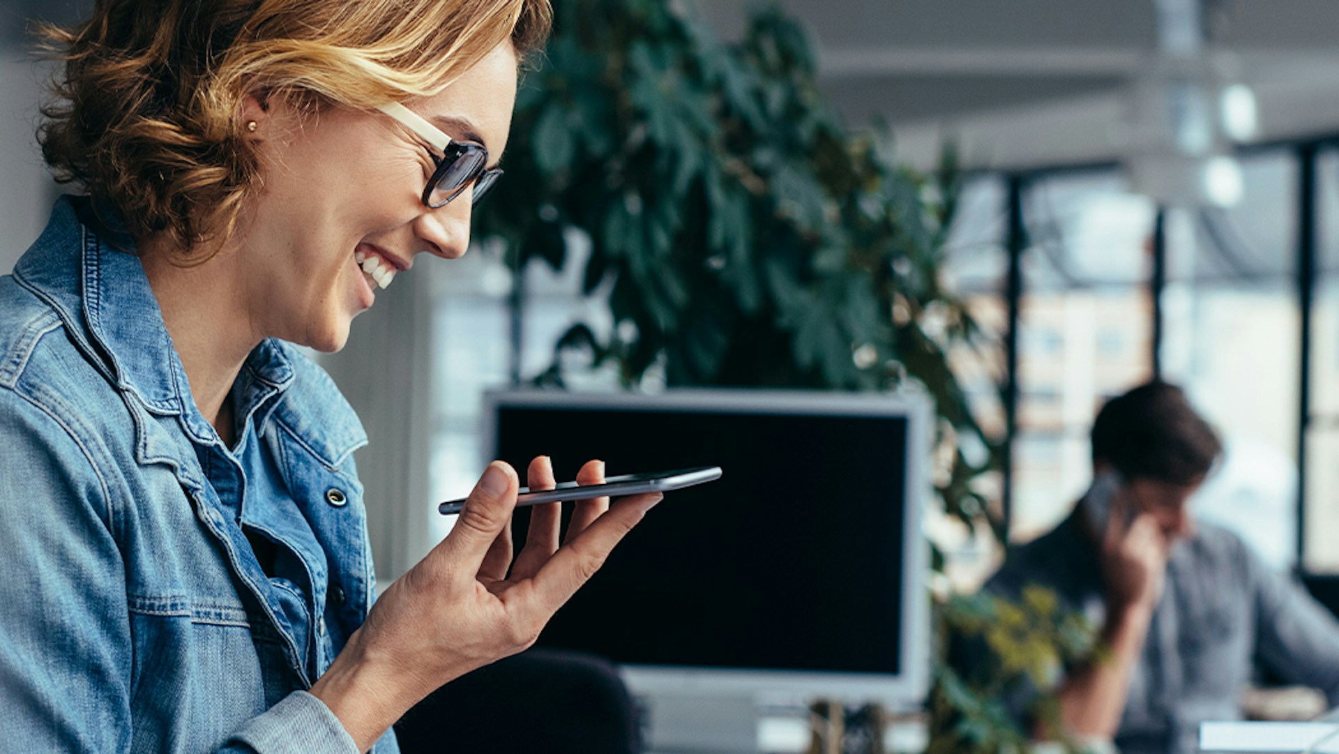 Woman in the office smiling and looking at her smartophone and a report