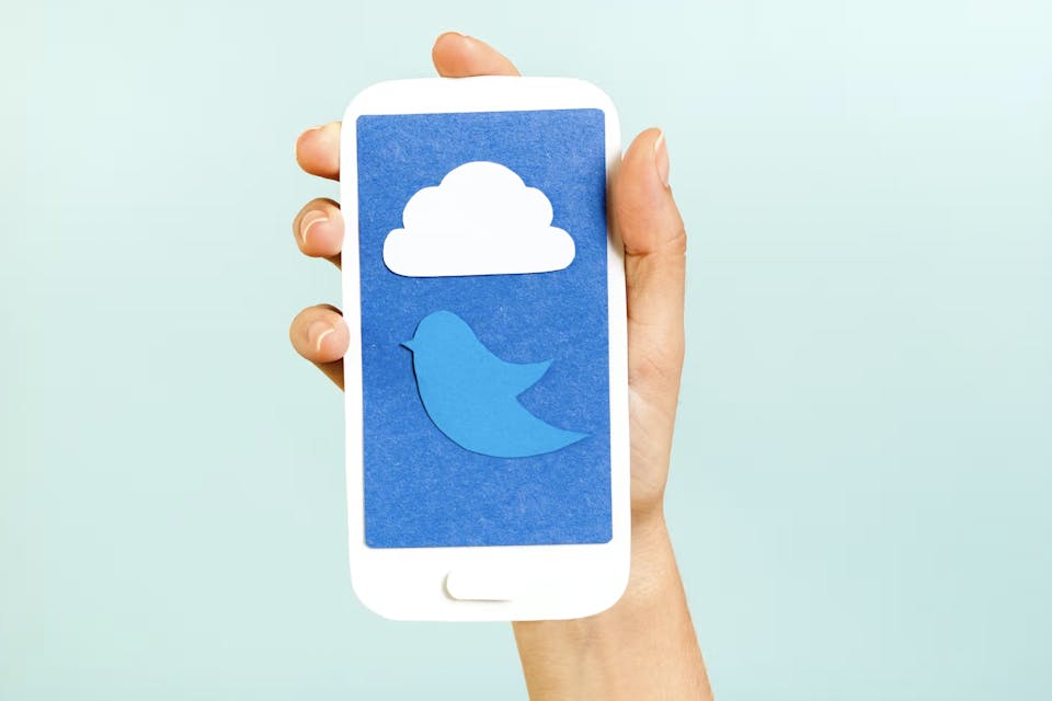 Twitterロゴの鳥や雲を表示したスマートフォンのペーパークラフトを持っている手元の画像