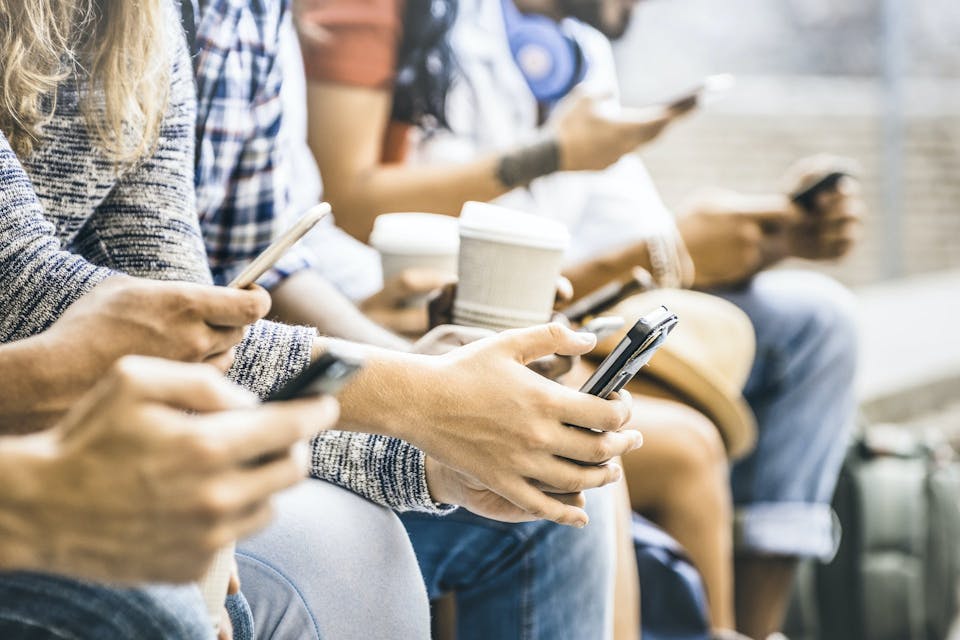 Foto von Jugendlichen, die nebeneinander sitzen und auf ihren Smartphones scrollen