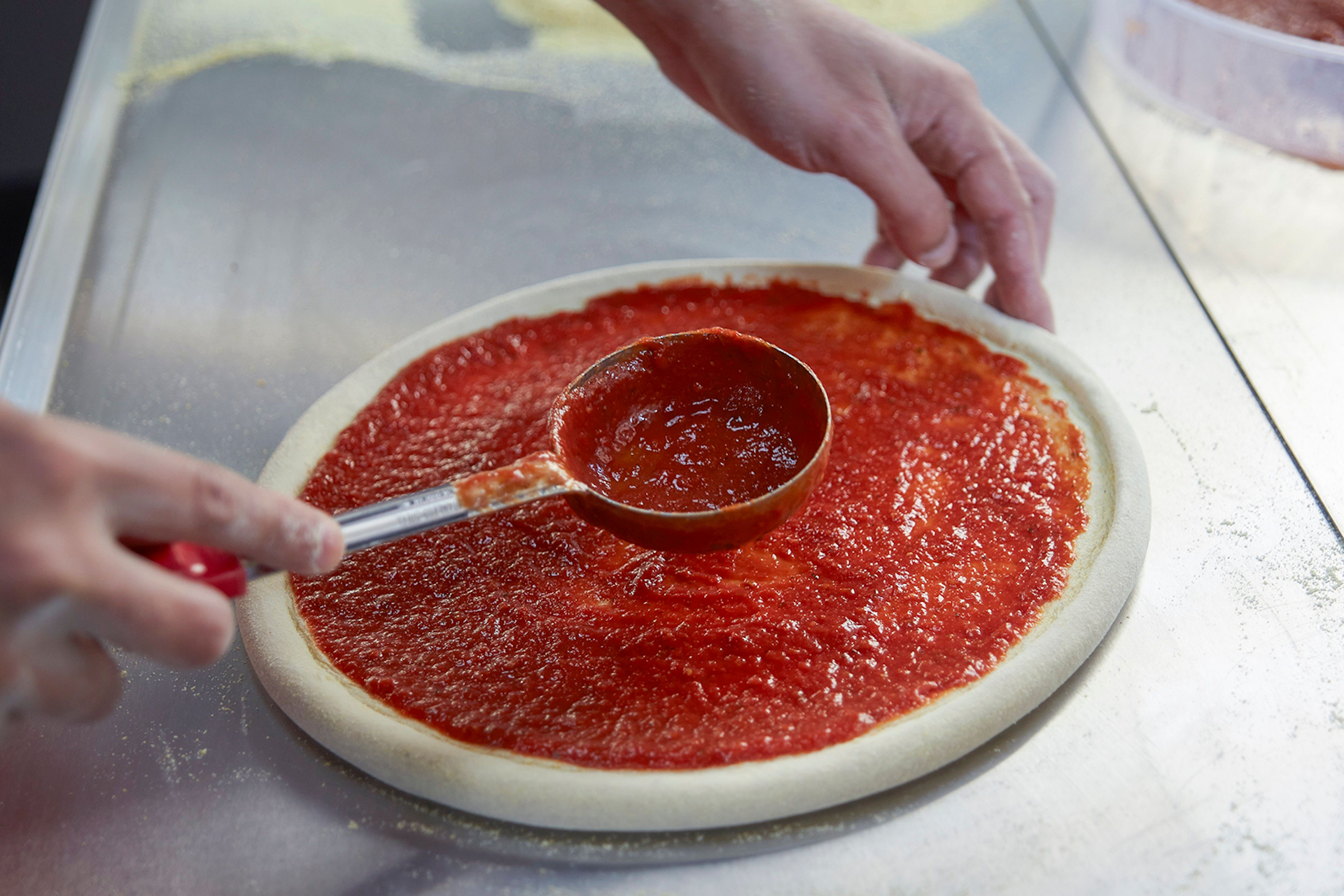 An image of someone spreading tomato sauce on a pizza base. This image is being used for a customer story explaining how Meltwater aids Domino's with its social media strategy. 