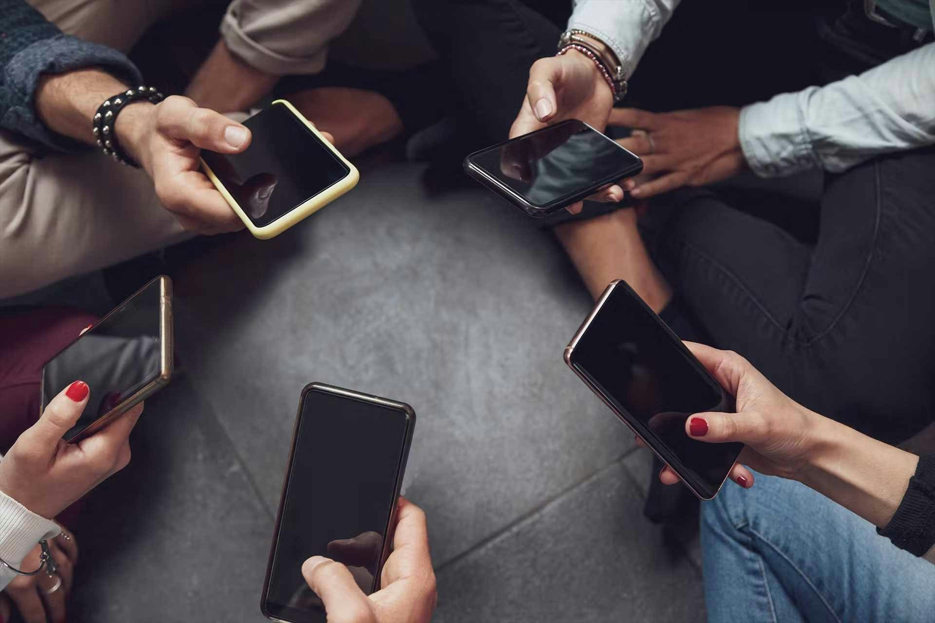 5 personnes assises en tailleur en cercle qui tiennent chacune un smartphone dans leurs mains