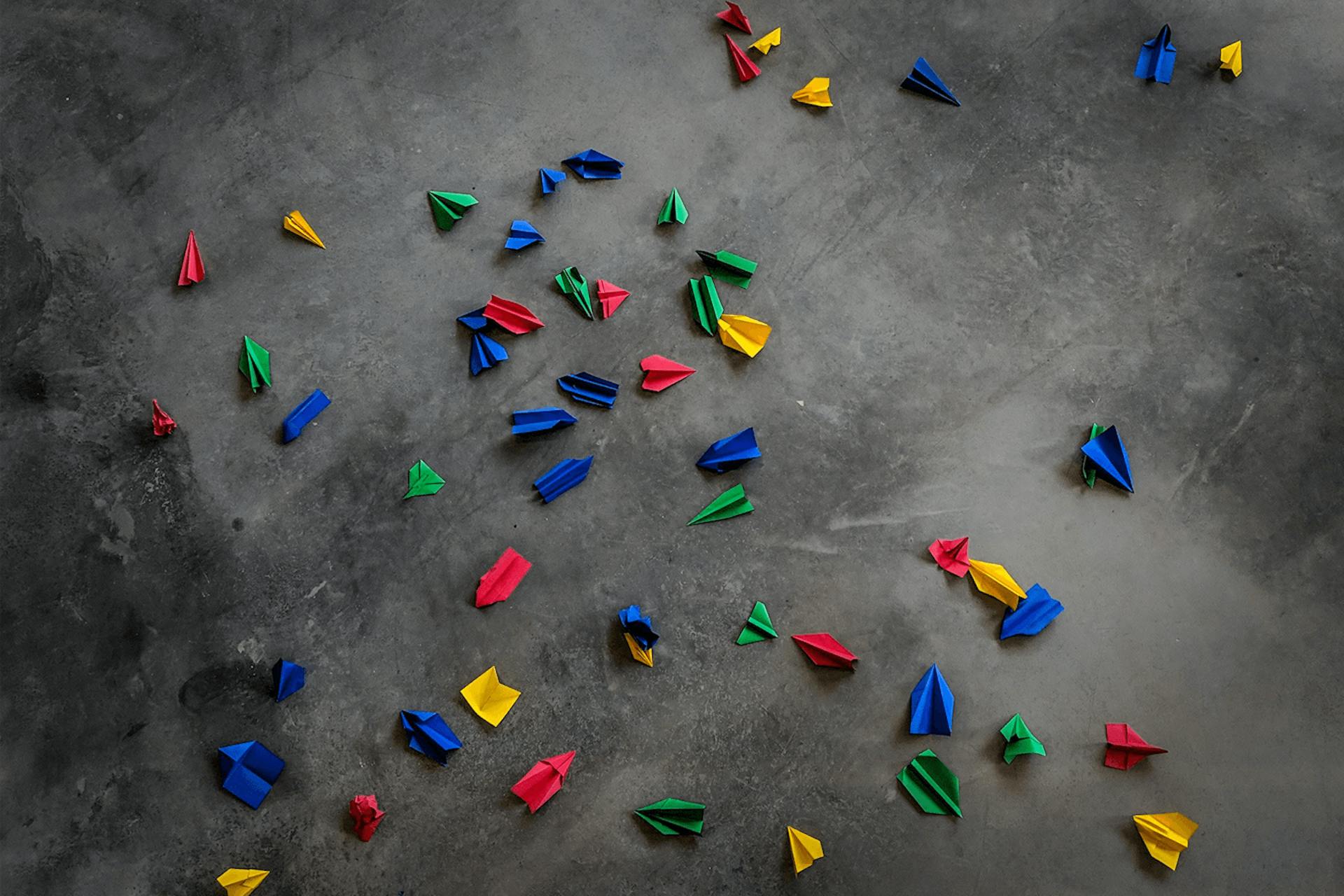 Foto grauer Hintergrund mit bunten Papierfliegern in Google Farben