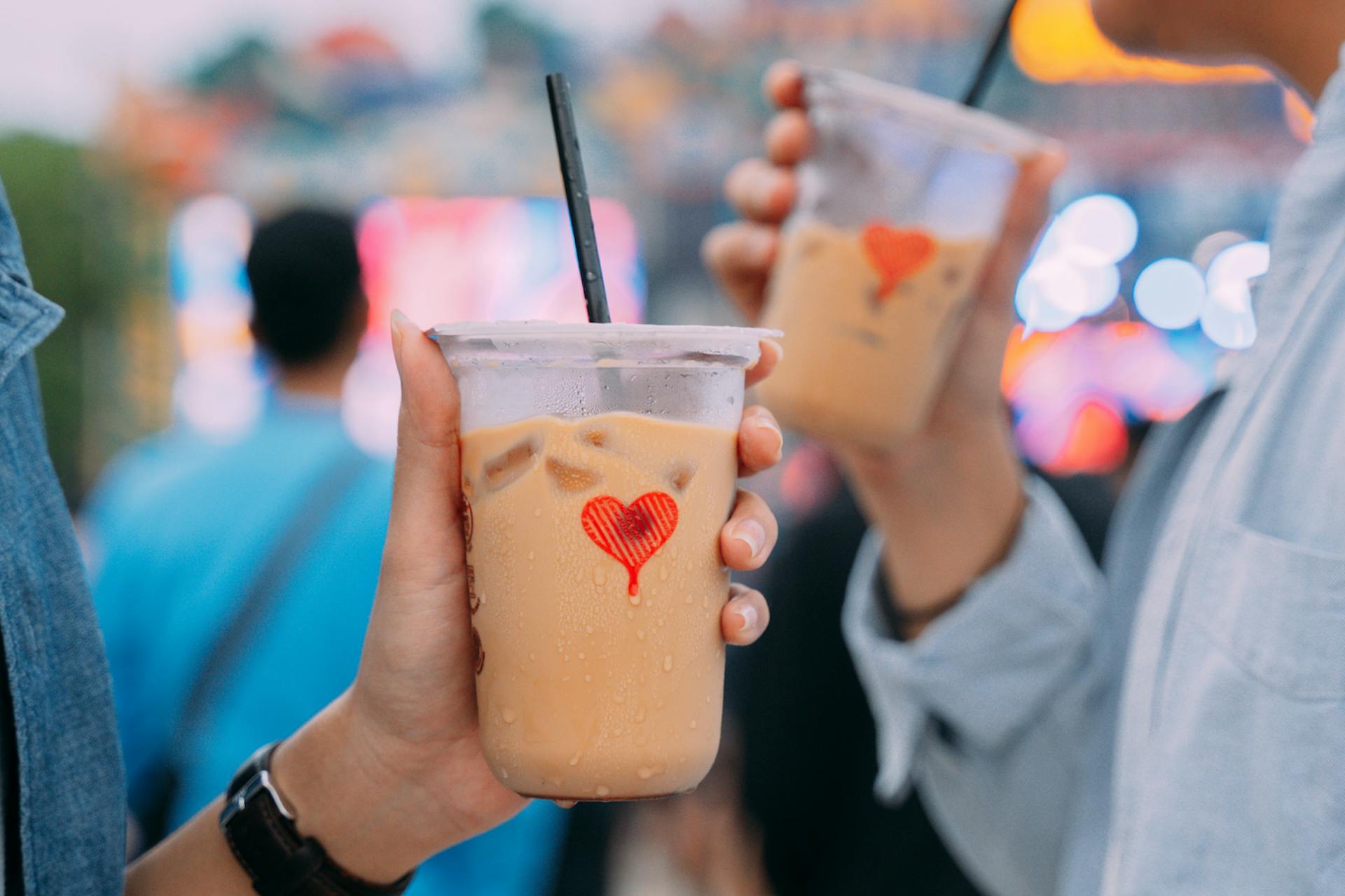 Two people almost facing one another are holding a cup of Kopi Kenangan coffee each 