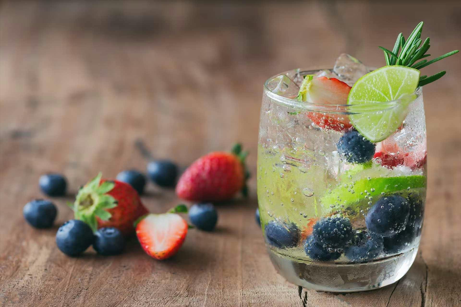 Verre d'eau remplie de fruit, posé sur une table en bois avec des fruits à côté 