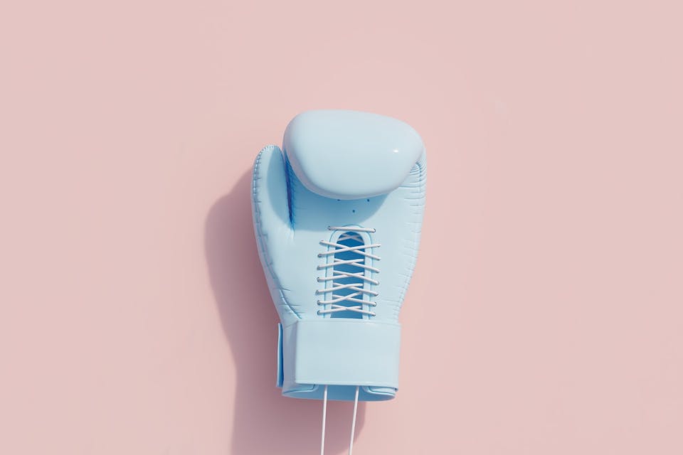 A blue boxing glove against a solid pink background. This guide will help you understand the concept of Competitive intelligence and how CI can benefit your business so you can fight off the competition