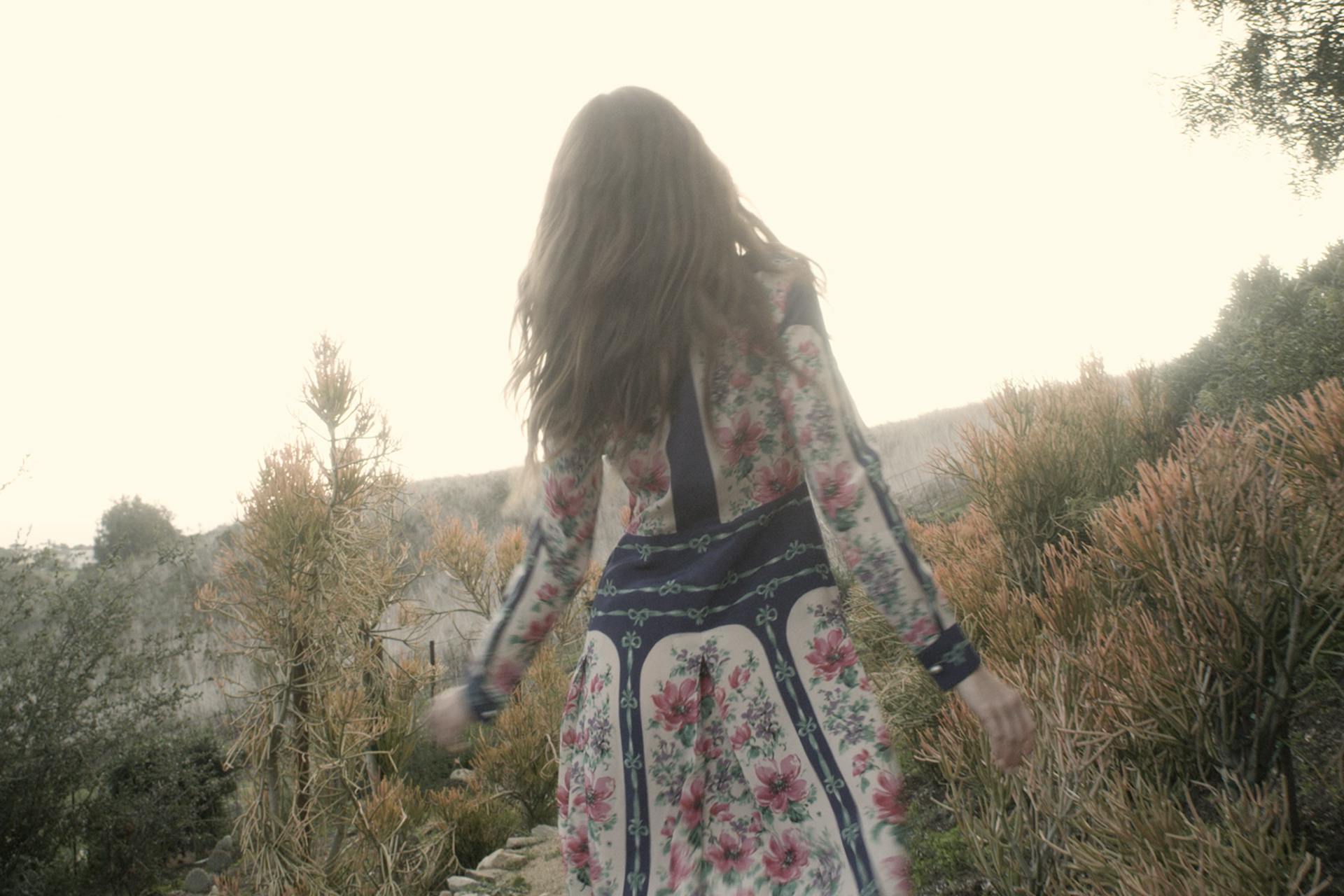 A photograph of woman in a floral dress from behind walking in a desert