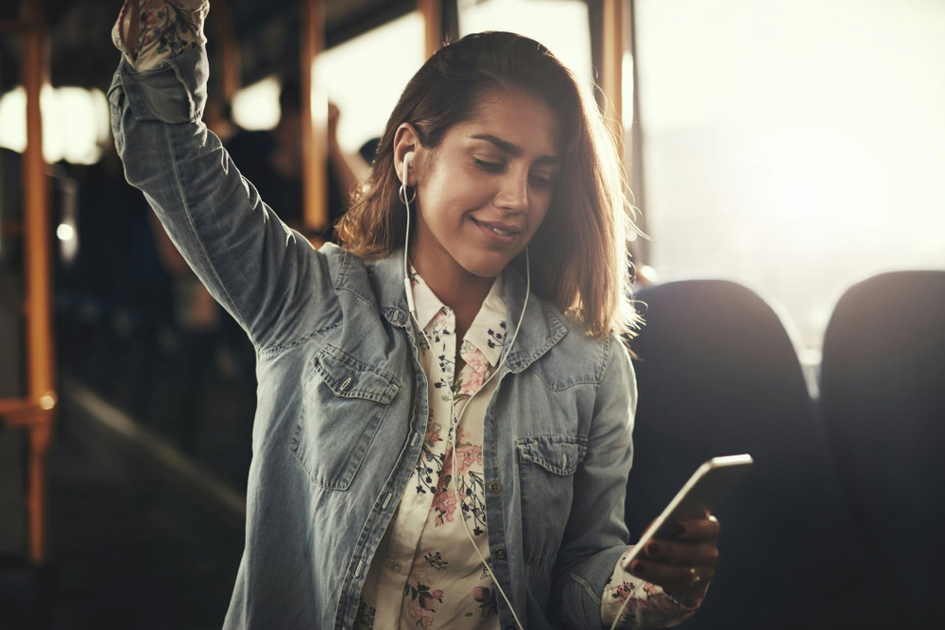 Eine junge Frau steht mit ihrem Smartphone im Bus