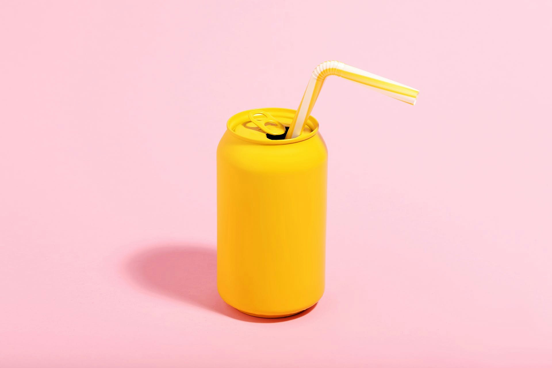 Bright yellow soda can with straw, on pink background. Blog post on definition of brand ambassadors