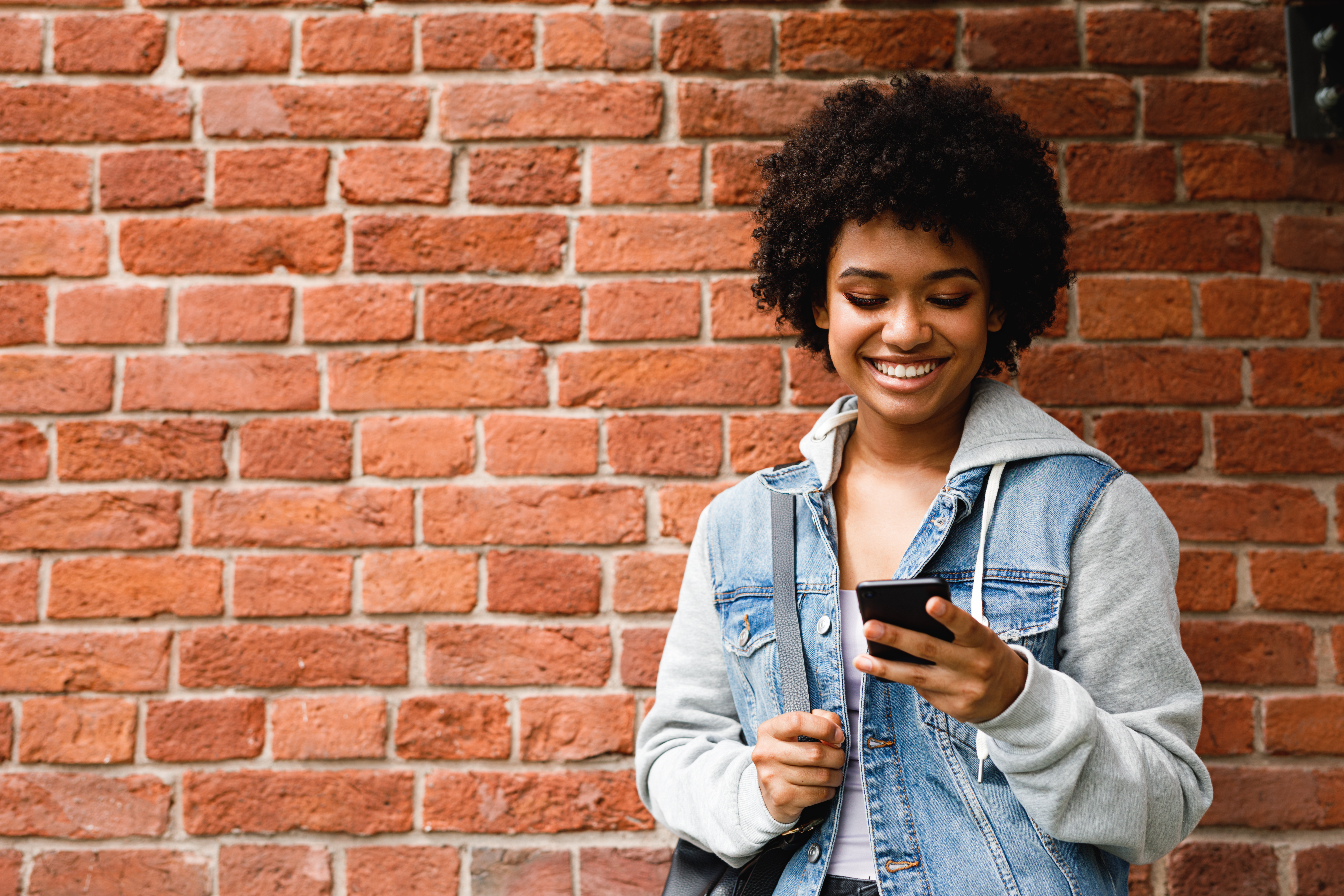 photo of a woman with her smartphone in hand standing in front of a brick wall