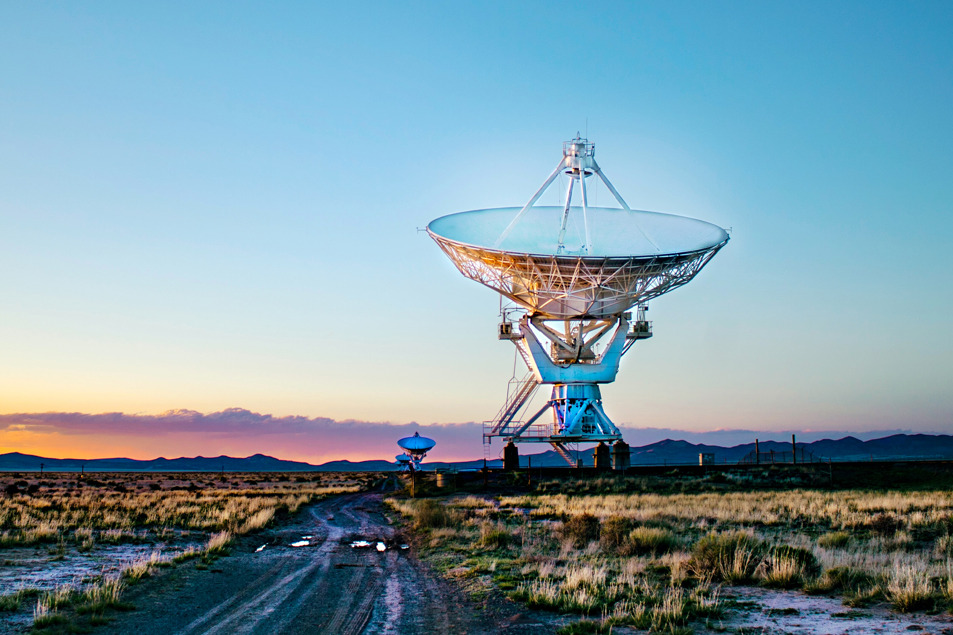 An image of a satellite dish in a field pointed up towards the sky at sunset
