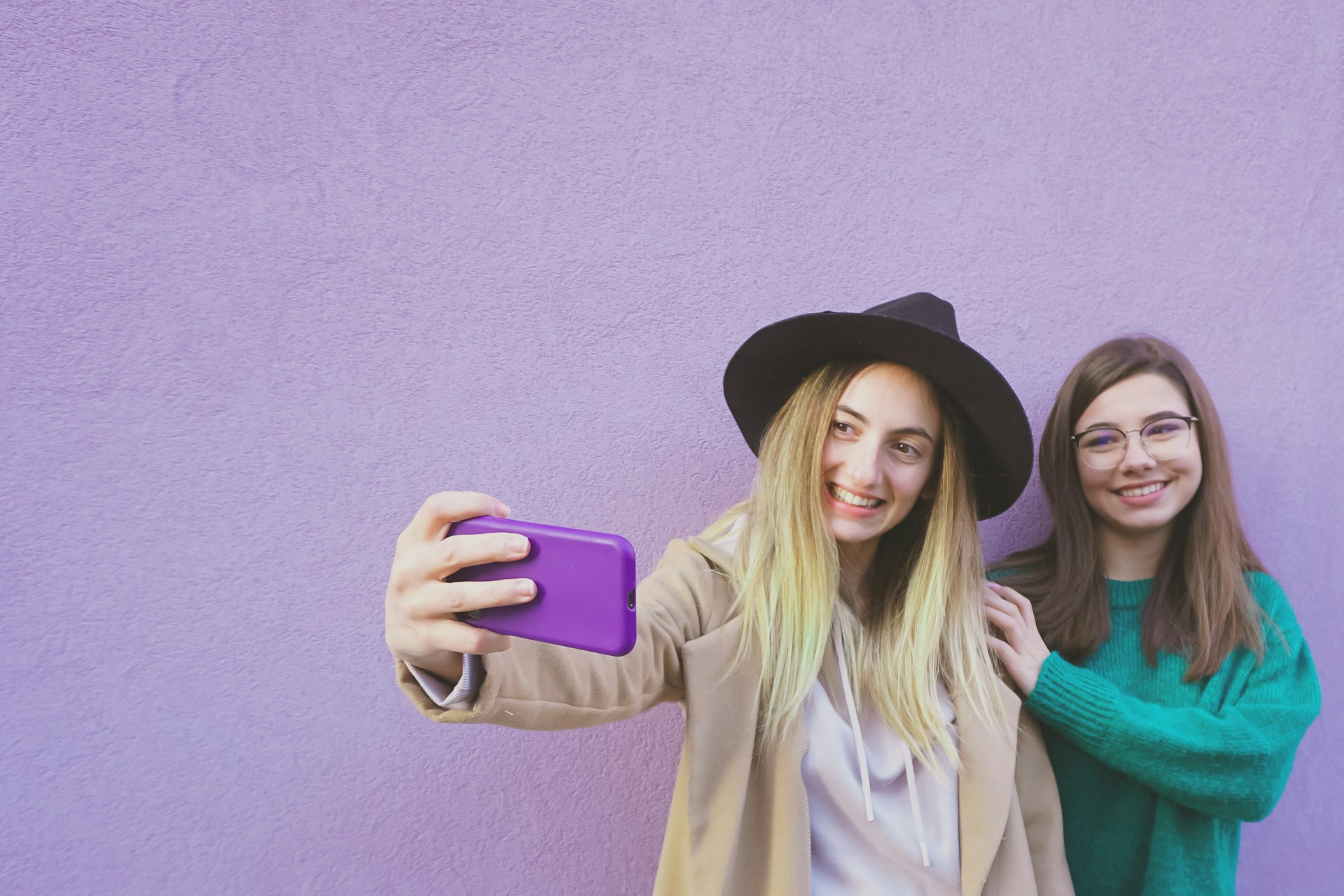Two young girls, taking a selfie in front of a purple wall. 