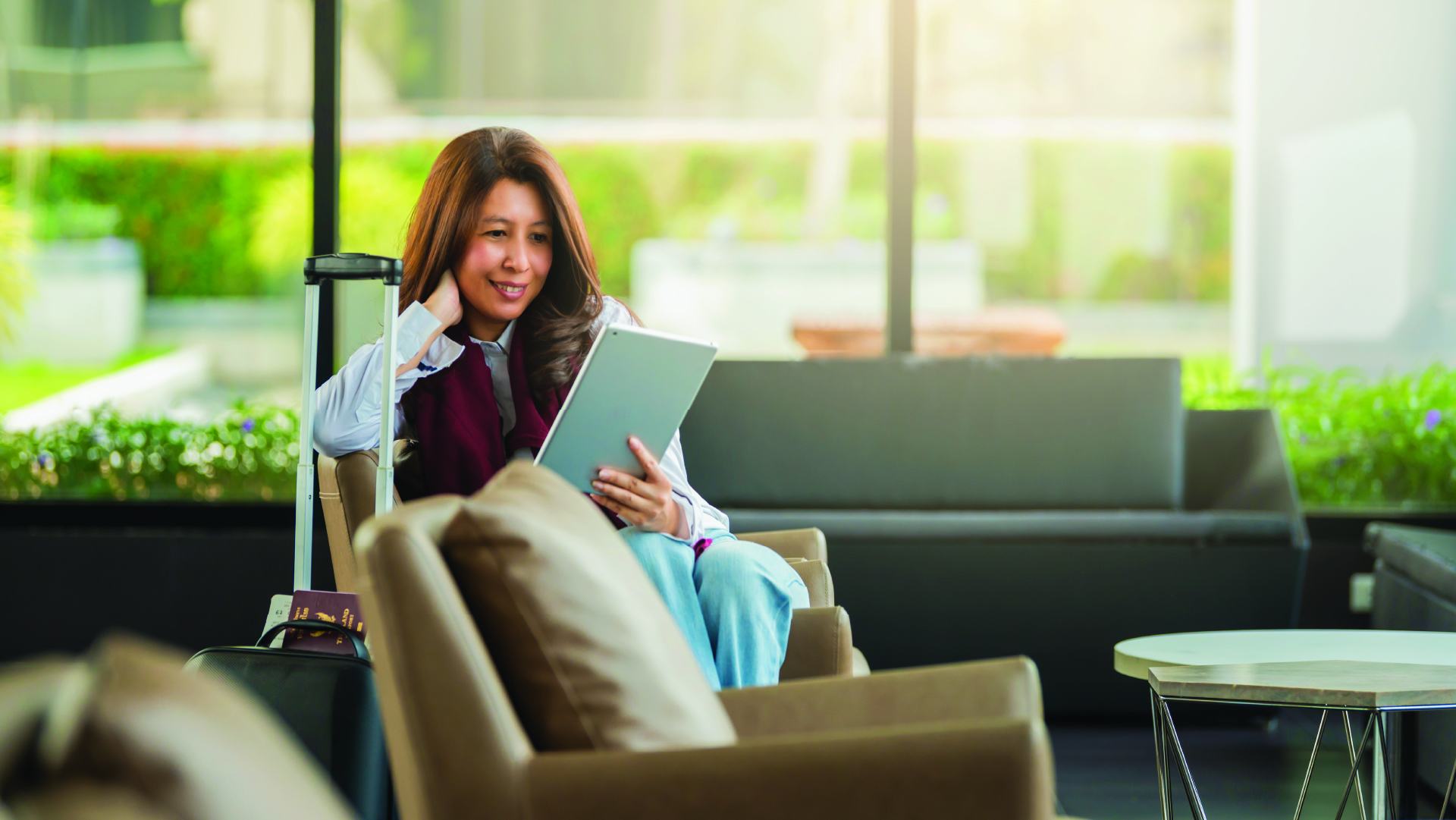 A woman using a tablet while sitting in a hotel lobby with her luggage