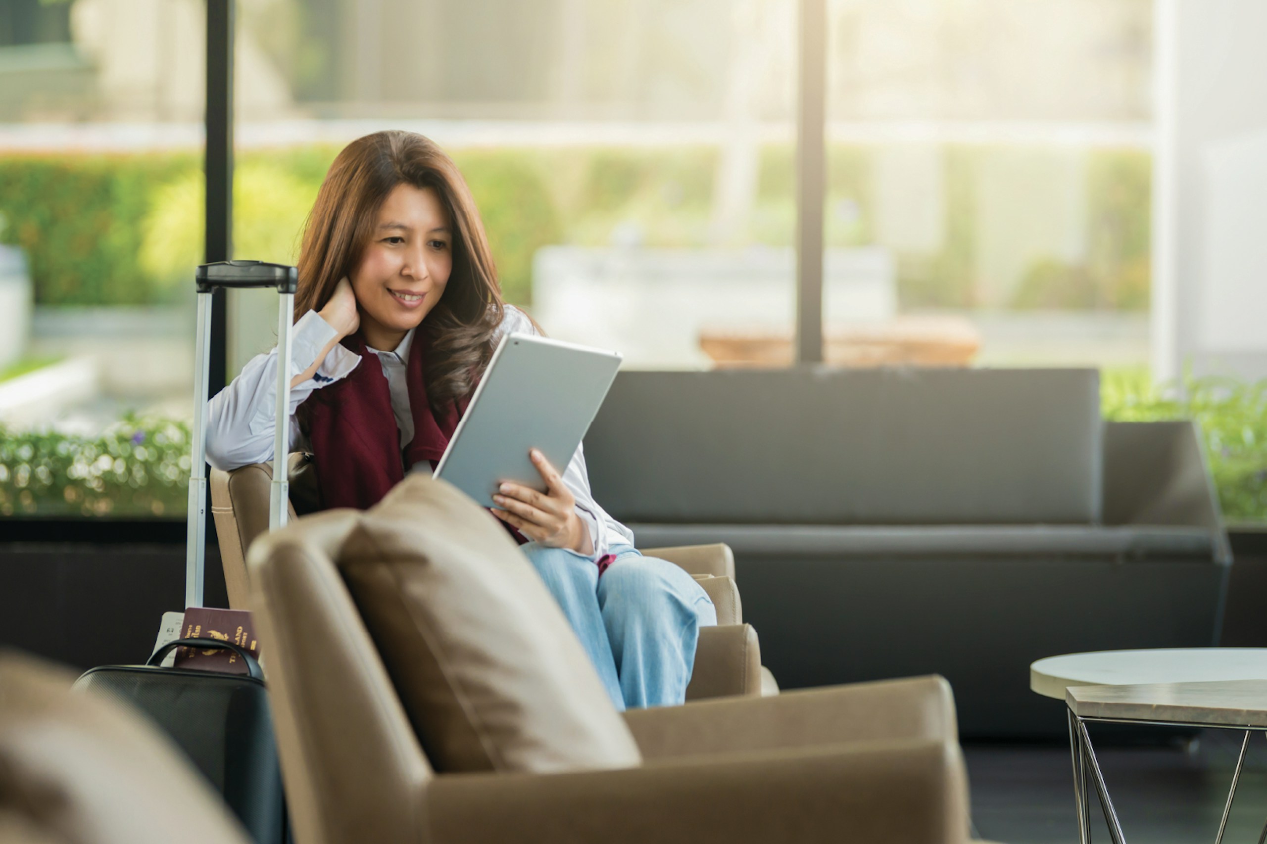 A woman using a tablet while sitting in a hotel lobby with her luggage