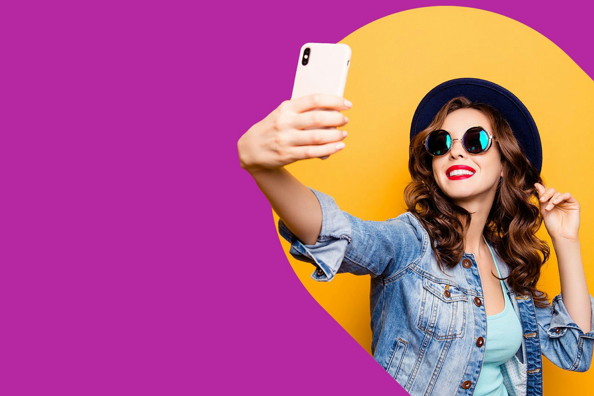 A female influencer in sunglasses and a hat taking a selfie for her social media followers. 