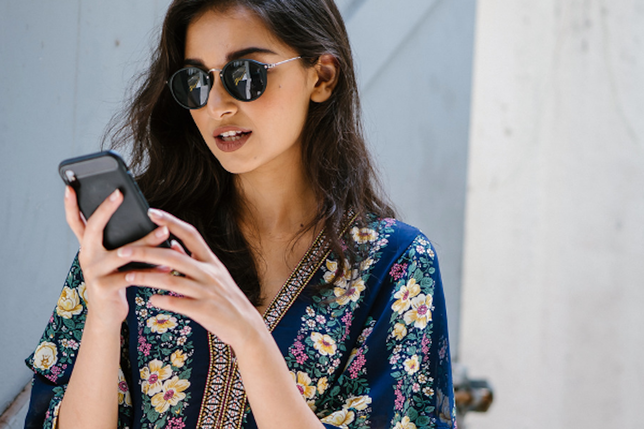 A woman in a colourful floral jacket playing on her phone.