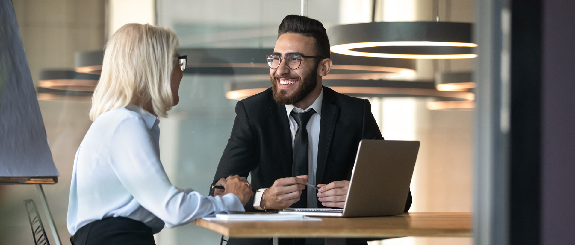 Two people, a man and a woman, sitting at a table in an office in front of a laptop