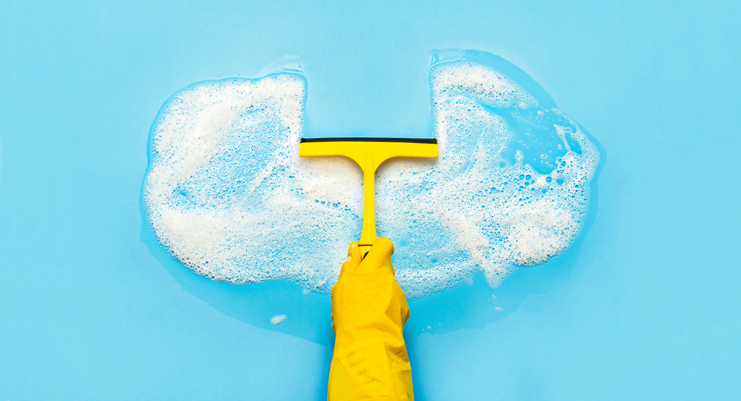 A person wearing a yellow glove holding a squeegee and wiping away a section of bubbles that are in the shape of a cloud. Today, most marketers store their customer data on a cloud-based software, which is why this image was selected for this blog by Meltwater on how to clean your cloud-based data. 