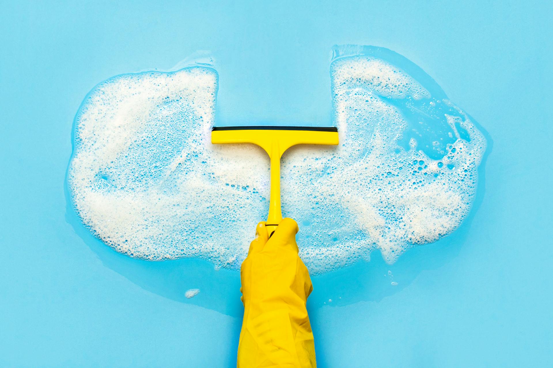 A person wearing a yellow glove holding a squeegee and wiping away a section of bubbles that are in the shape of a cloud. Today, most marketers store their customer data on a cloud-based software, which is why this image was selected for this blog by Meltwater on how to clean your cloud-based data. 