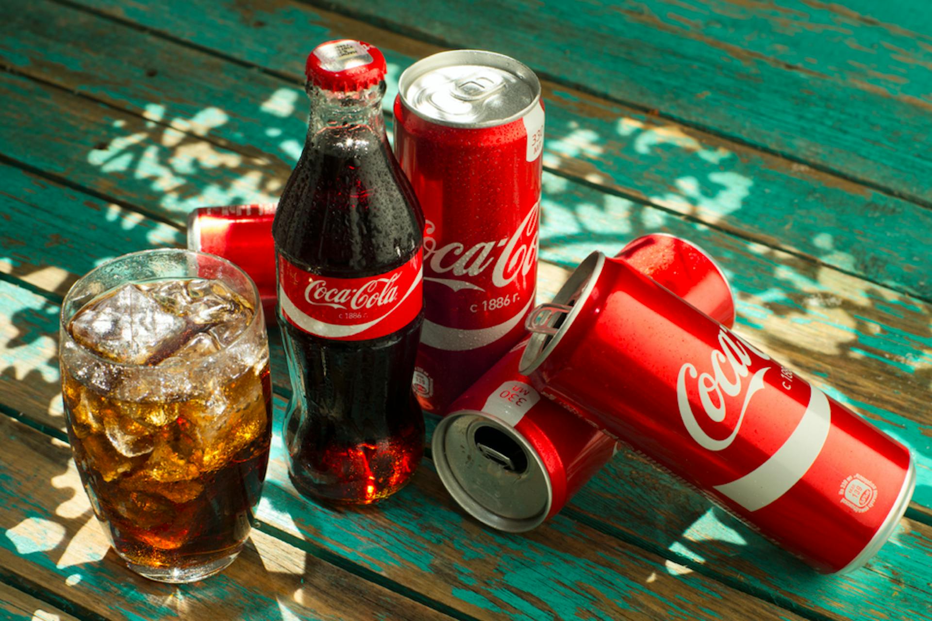 coca-cola can and glass bottle on a wooden table and glass with ice