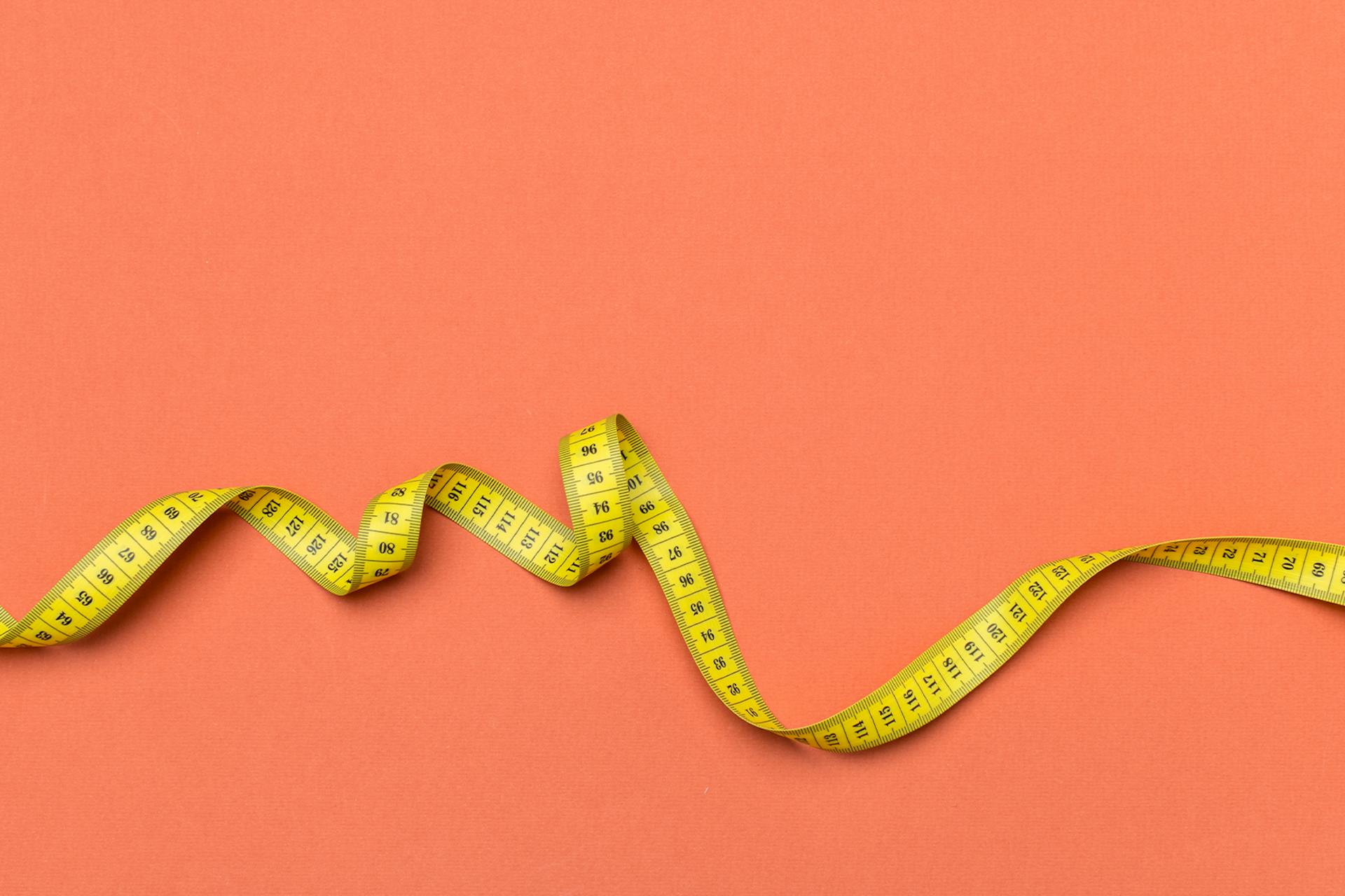 yellow tape measure against a coral pink background