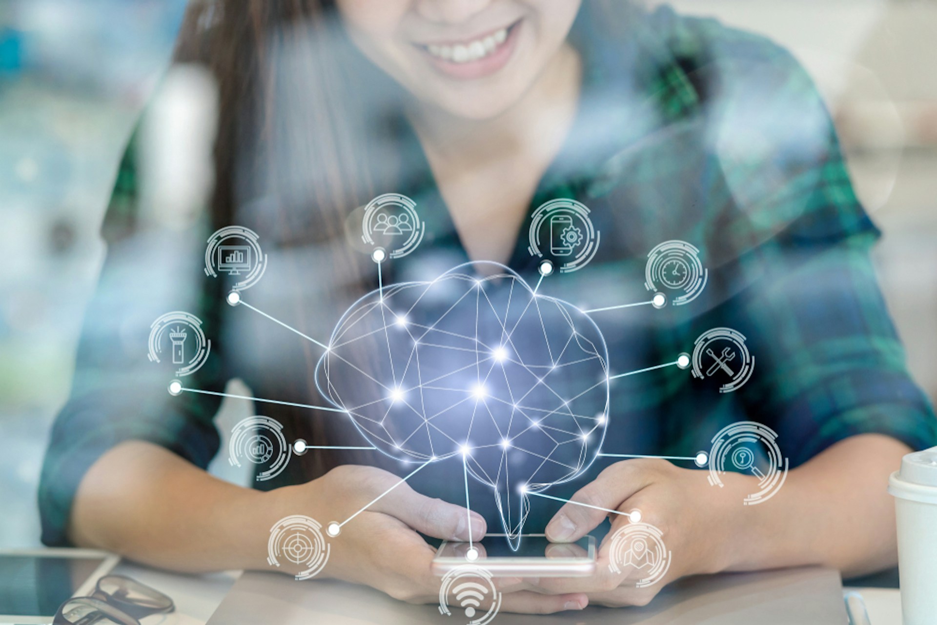 A data line illustration in the shape of a brain with technological icons against an image of a woman using her smartphone