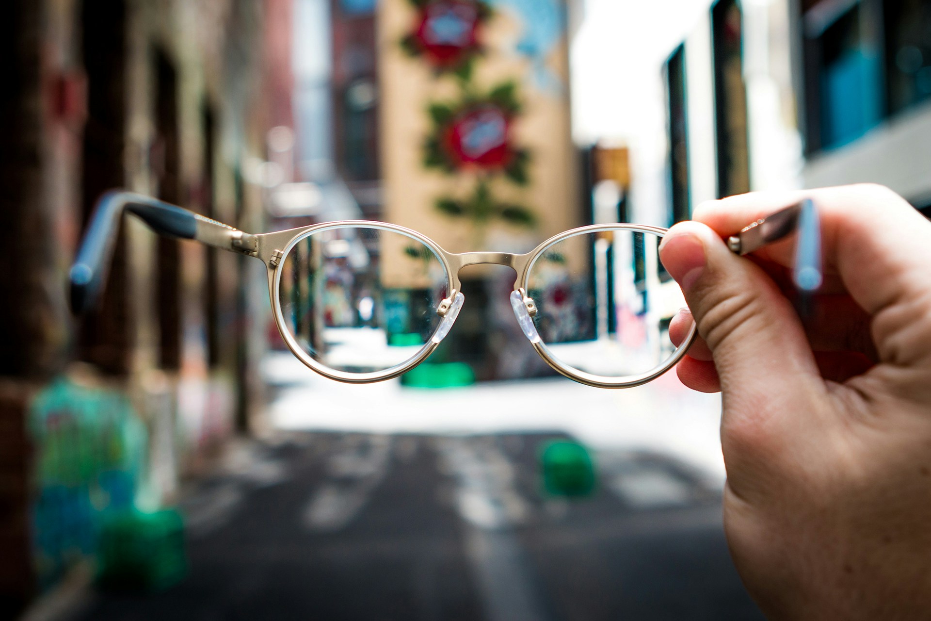 Person holding eyeglasses up to a brightly lit street. Header image for 10 steps for a social media audit.