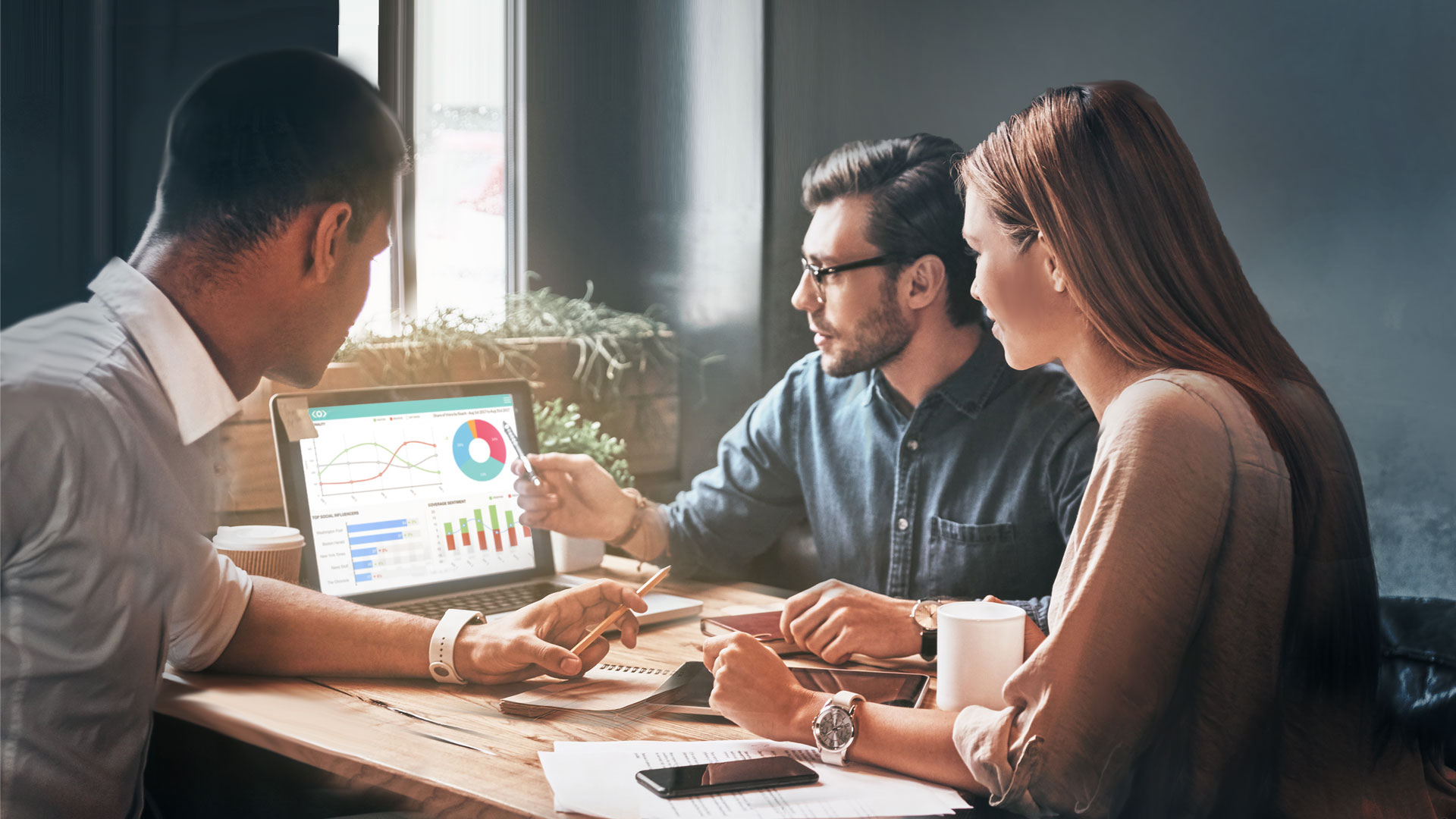 Photo of a team working on a laptop discussing Meltwater Media Intelligence dashboards
