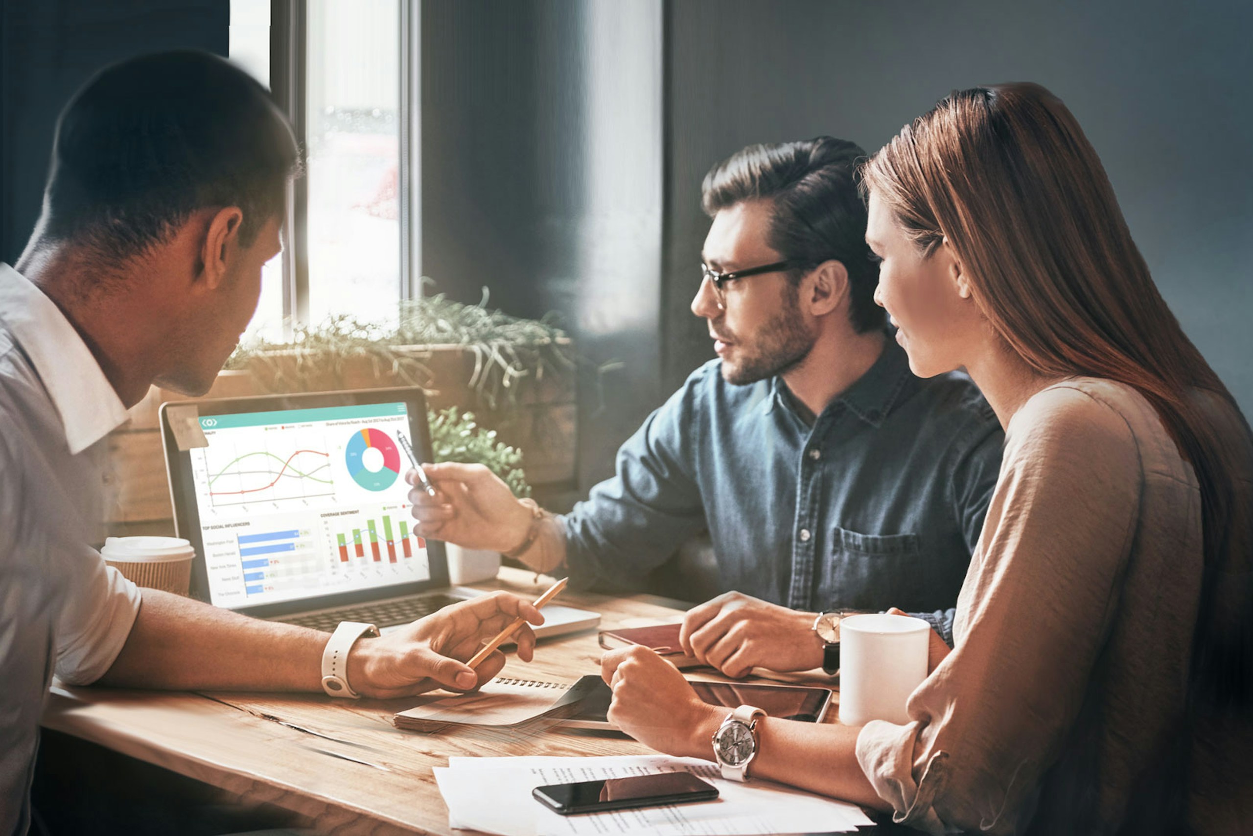 Photo of a team working on a laptop discussing Meltwater Media Intelligence dashboards
