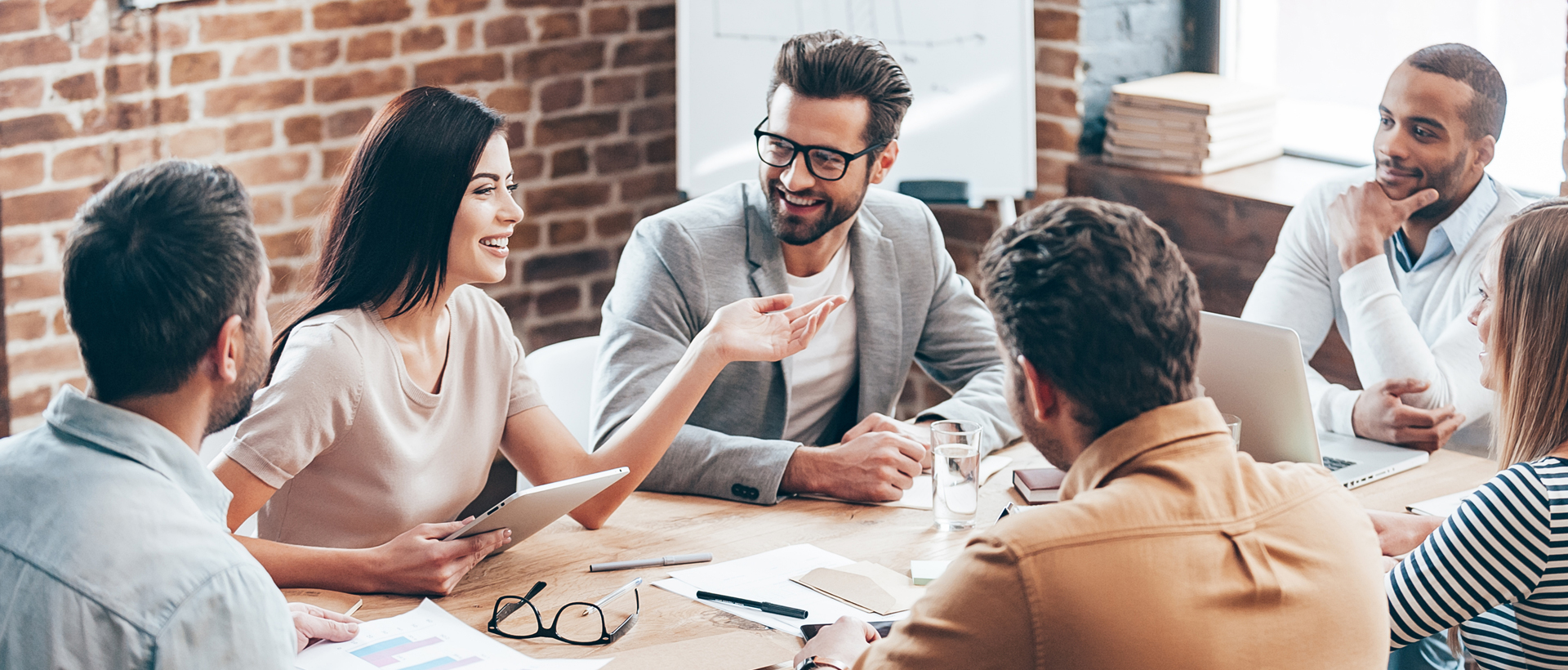 A group of diverse young professionals at an agency gathered around an office table having a meeting.
