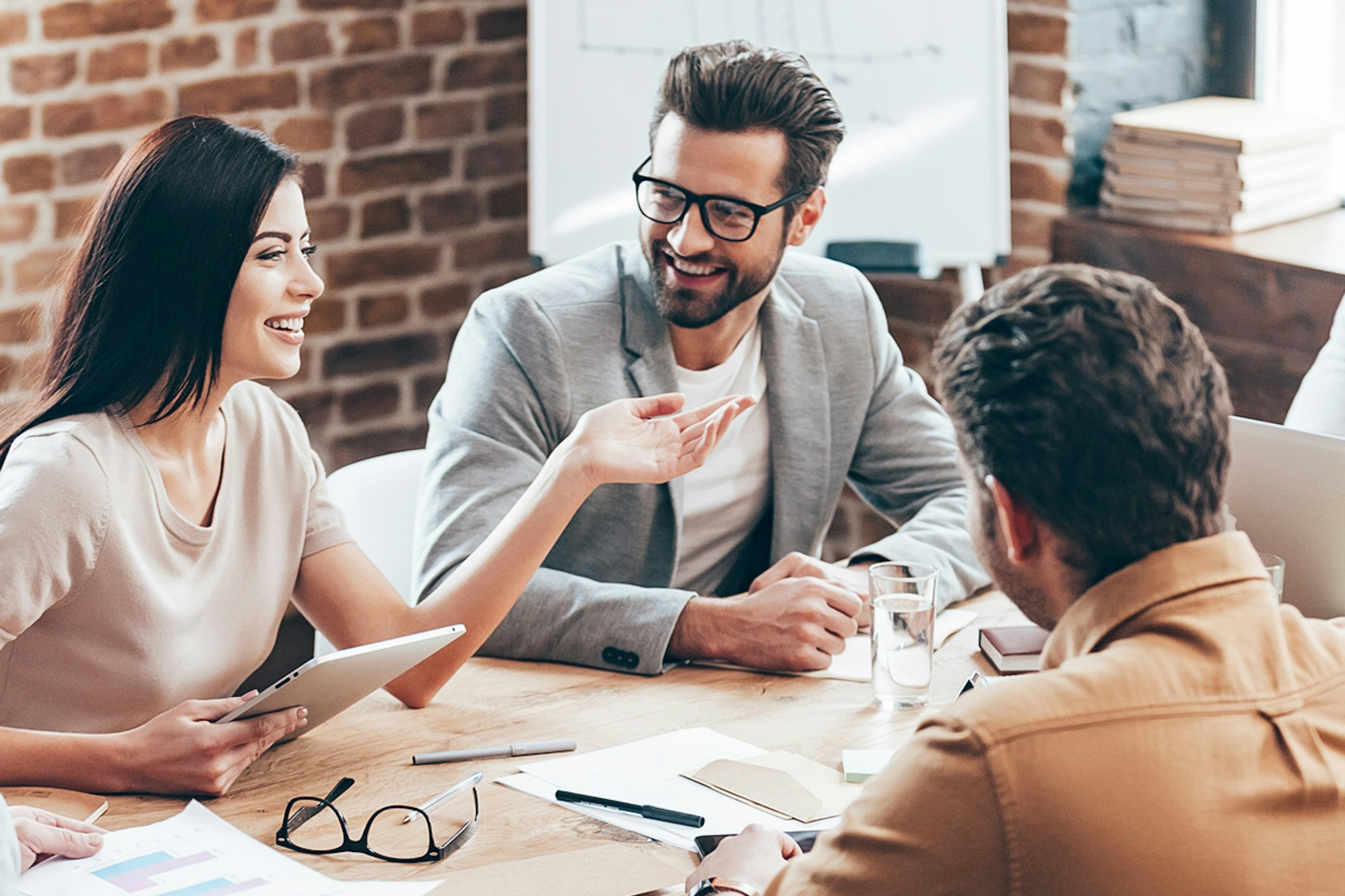 A group of diverse young professionals at an agency gathered around an office table having a meeting.
