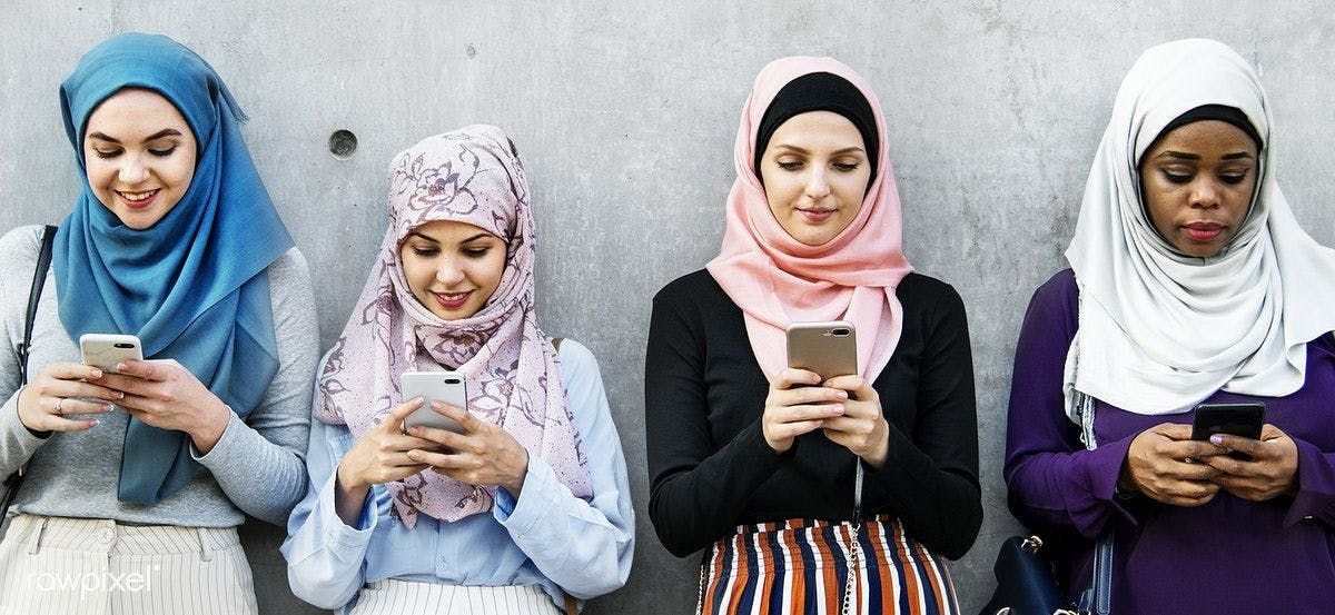 four arab women against a grey wall looking at their smartphones