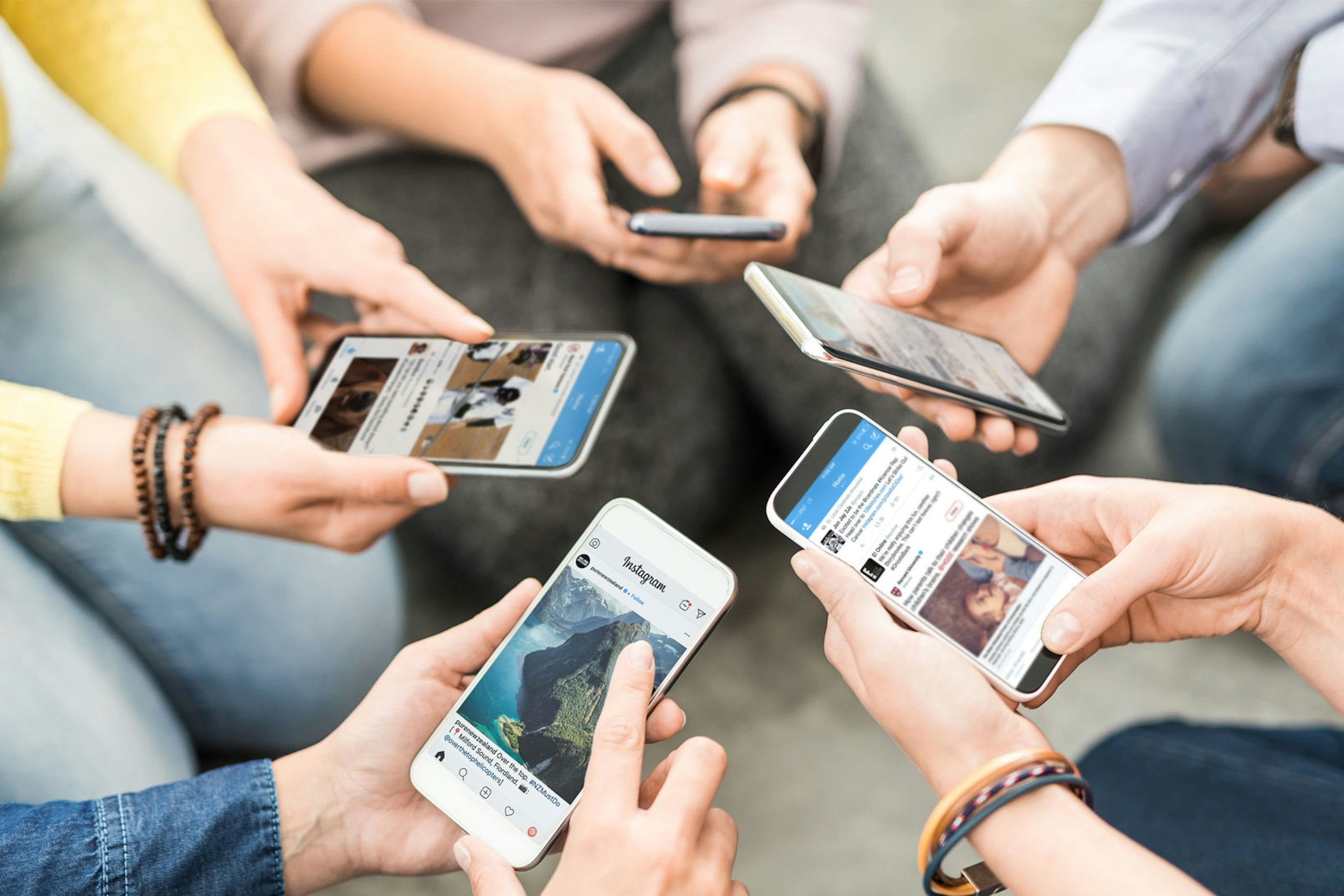 Photo of people sitting in a circle holding their smartphones into the middle