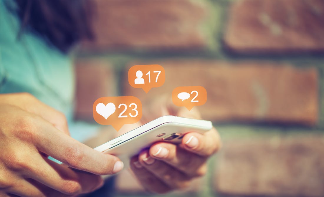 person holding a phone with like button, follower count and comment number speech bubbles