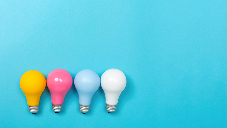 Yellow, pink, blue, and white lightbulbs laid side-by-side against blue background