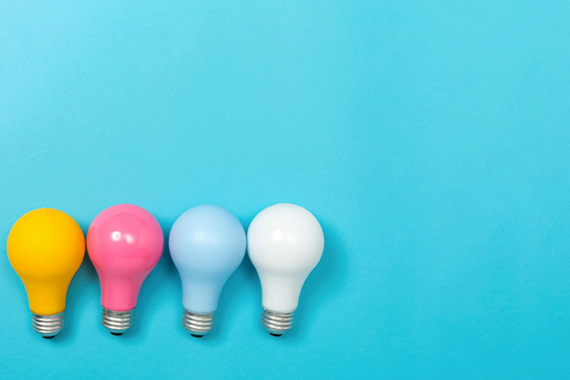 Yellow, pink, blue, and white lightbulbs laid side-by-side against blue background