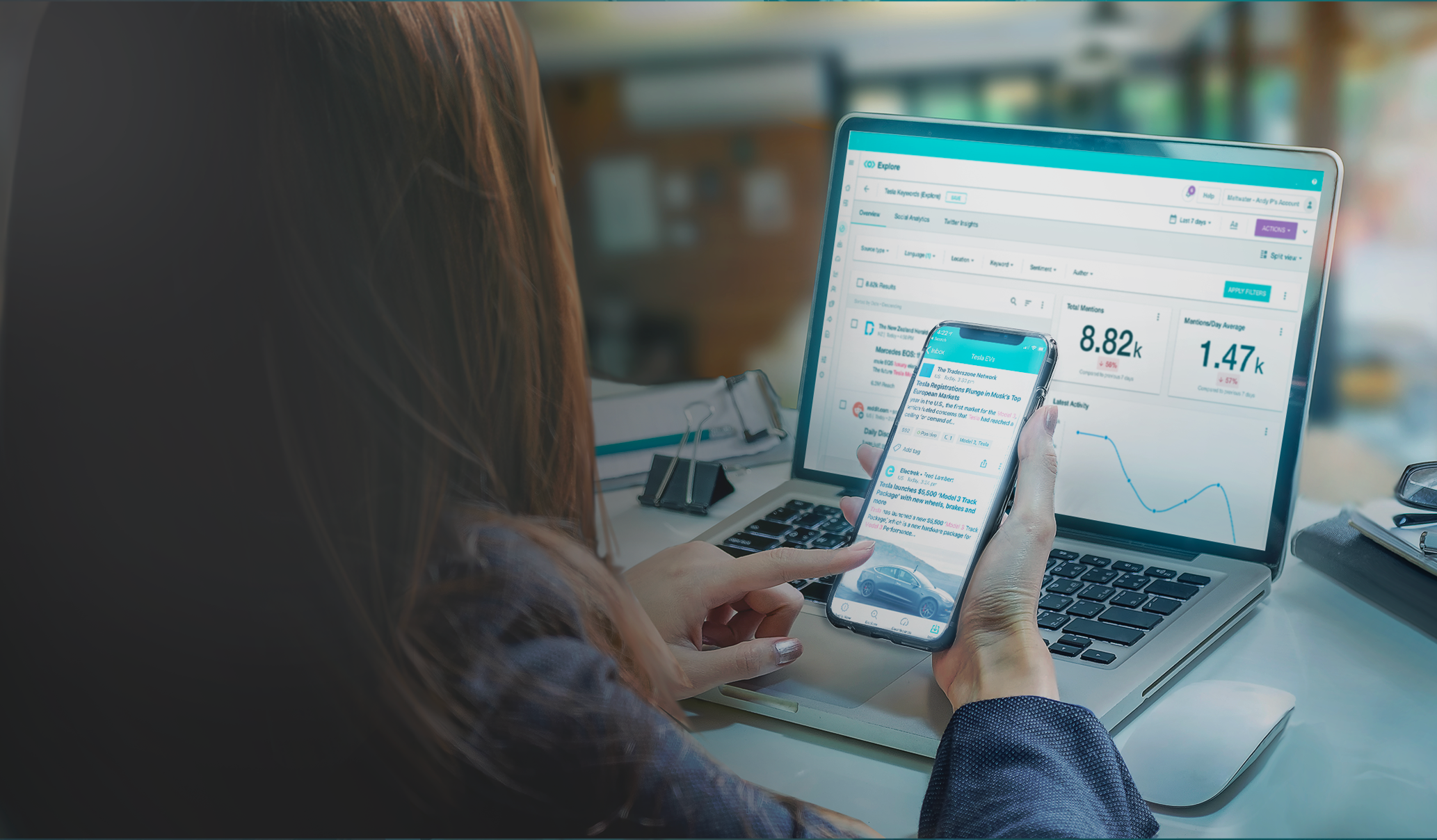 Woman at laptop, busy on her cell phone with a computer screen in the background. 