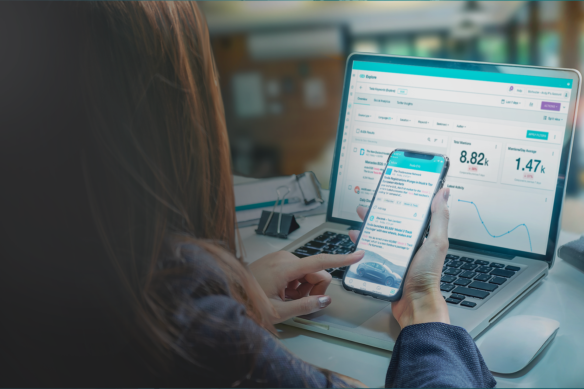 Woman at laptop, busy on her cell phone with a computer screen in the background. 